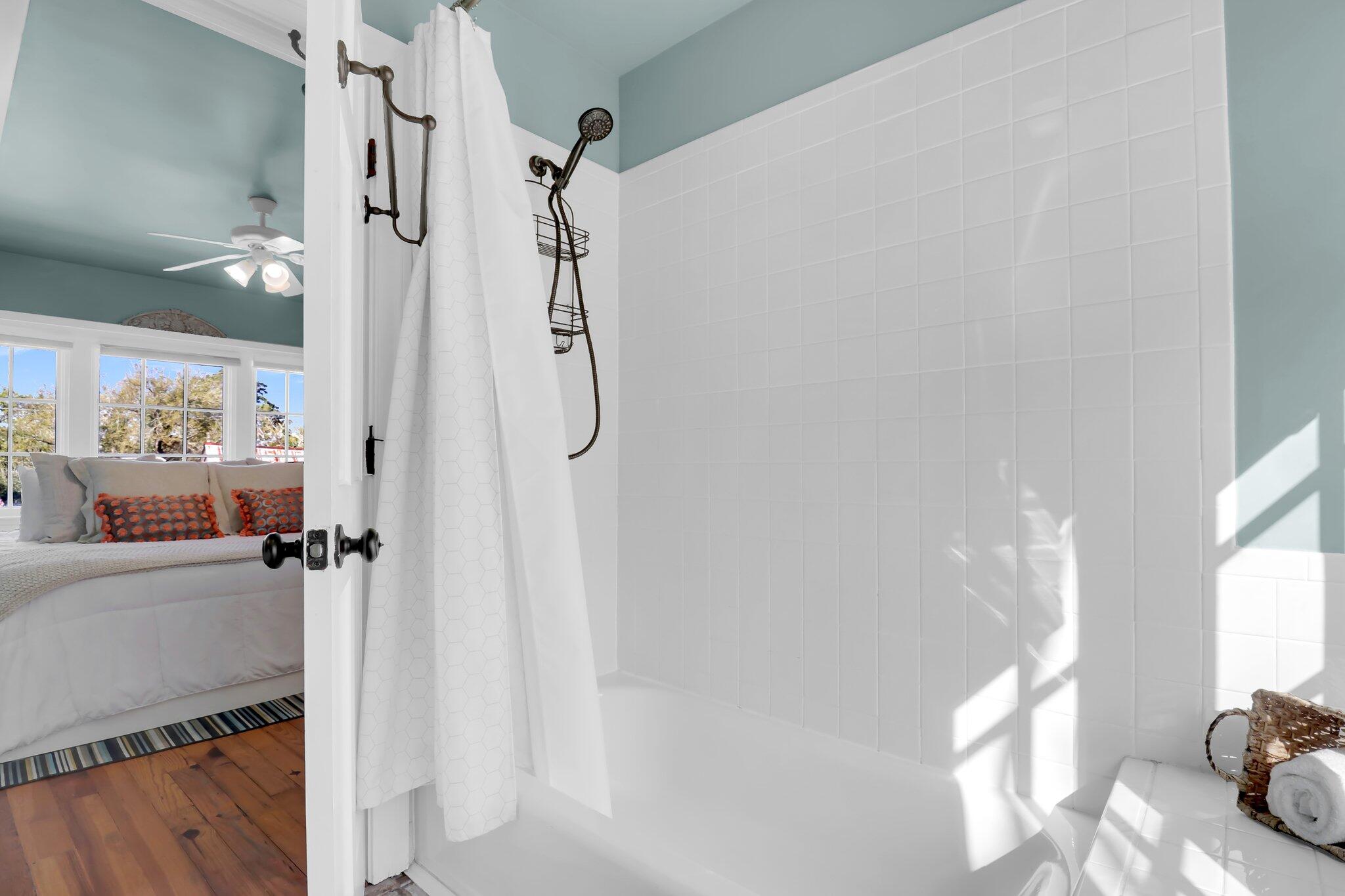 Bright tiled bathroom with bronze shower fixtures and a glimpse of the adjacent bedroom.