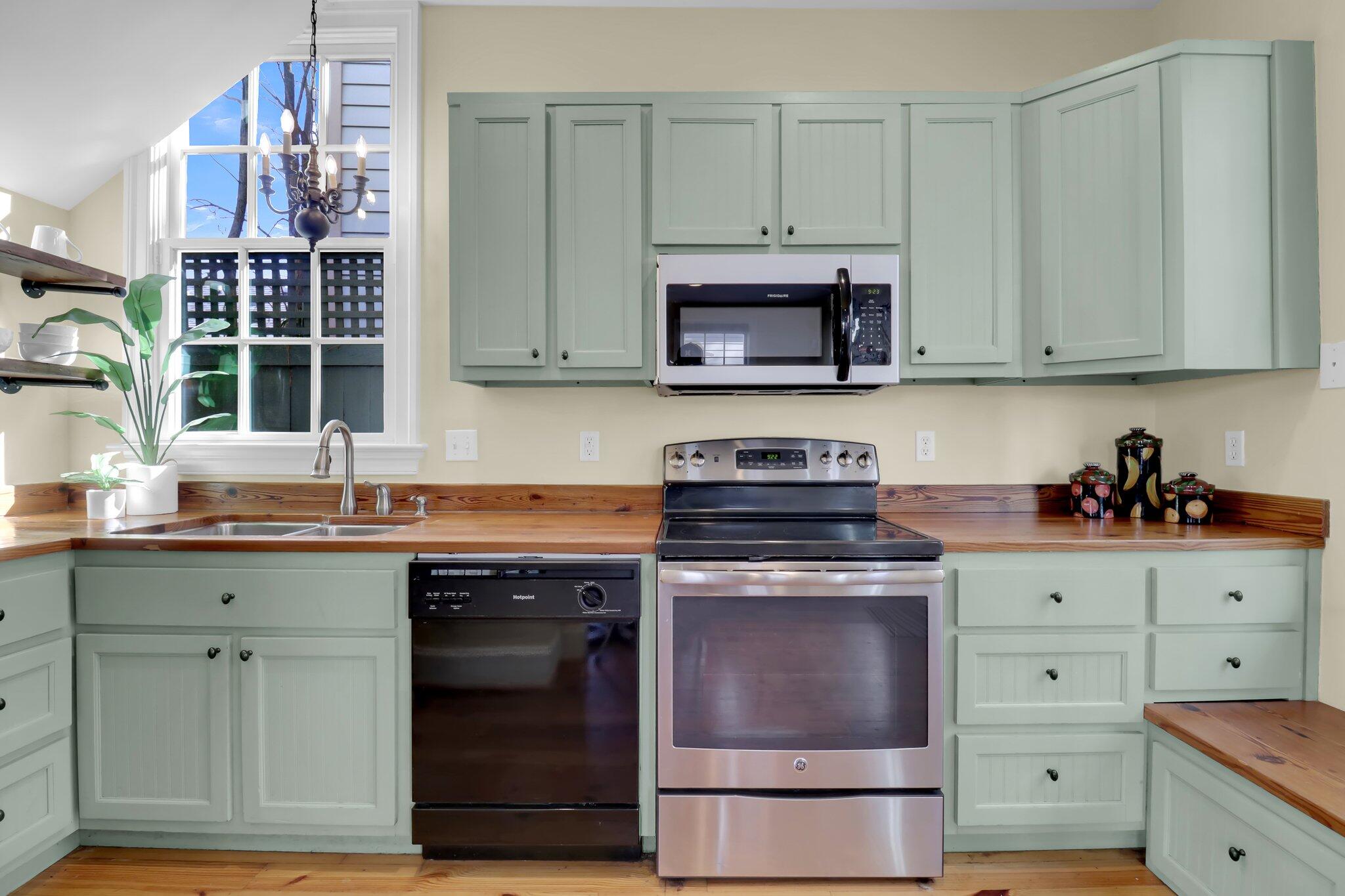 Kitchen with sage-green cabinets, wood countertops, and a tall window above the sink.