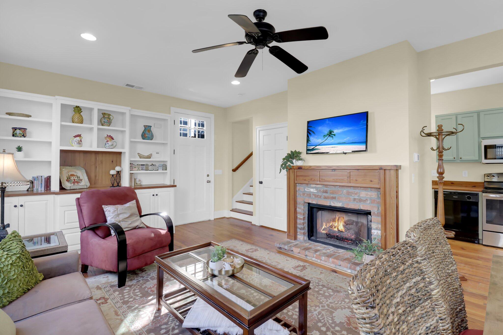Living room with built-in shelves, a brick fireplace, and an open kitchen.