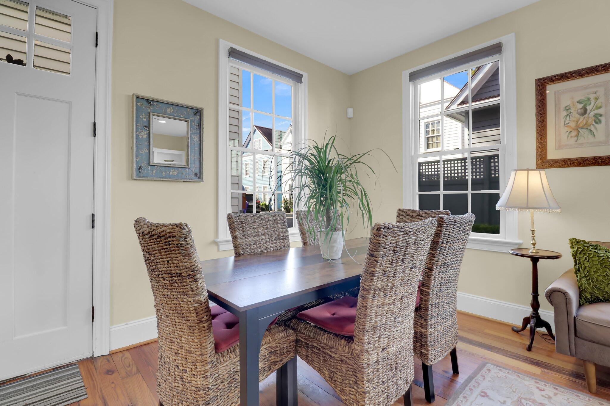 Dining area with woven chairs around a dark wood table beside tall windows.