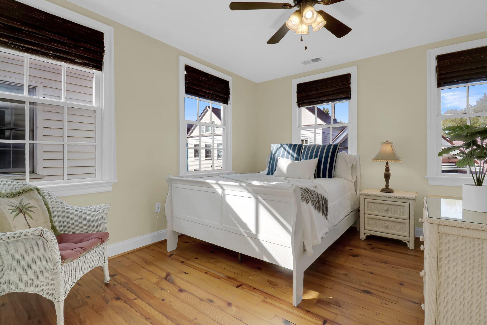 Bright bedroom with a white bed, blue striped pillows, wicker chair, and wood floors.