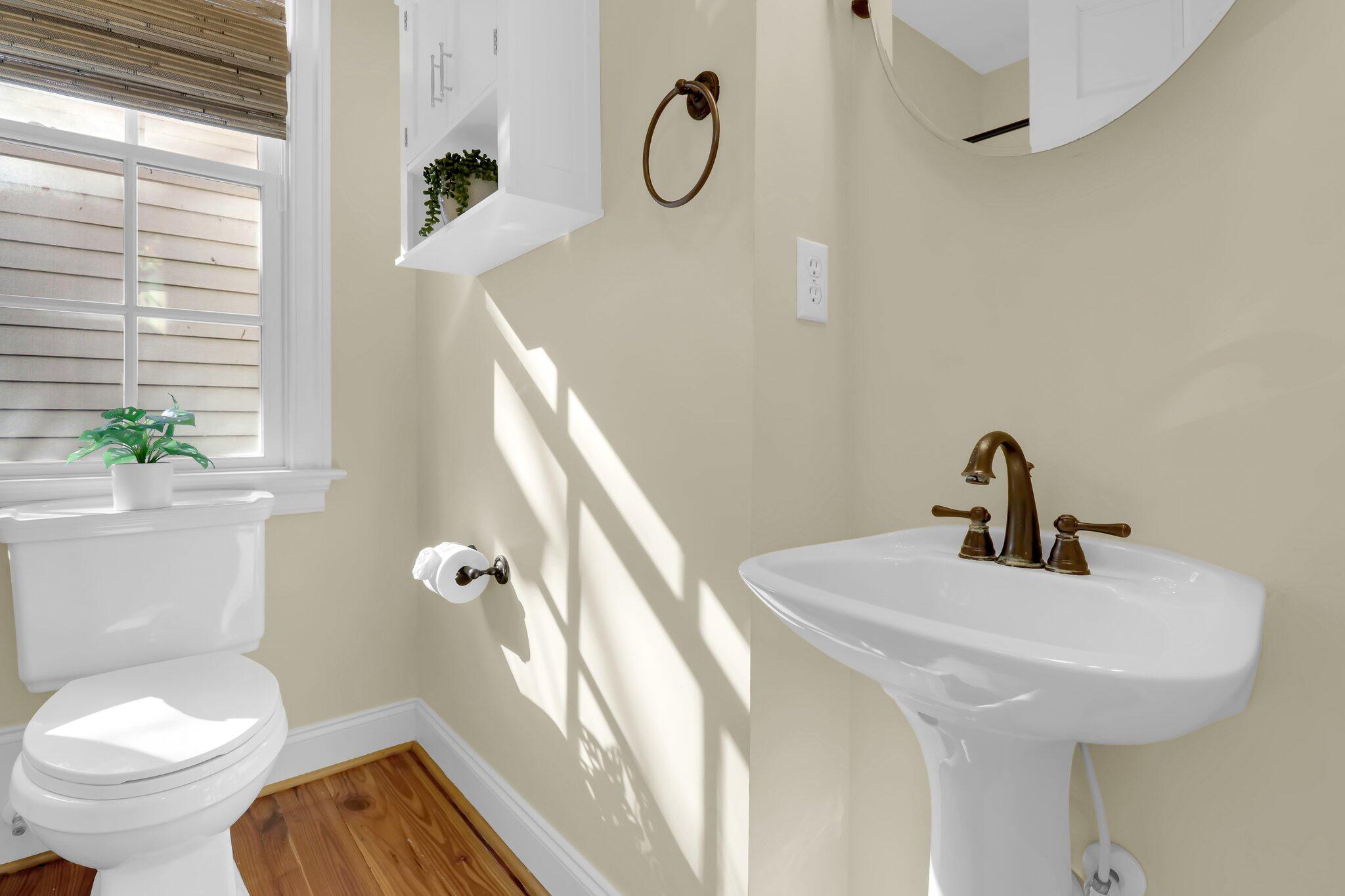 Bathroom with a pedestal sink and bronze faucet beside a toilet under a sunlit window.