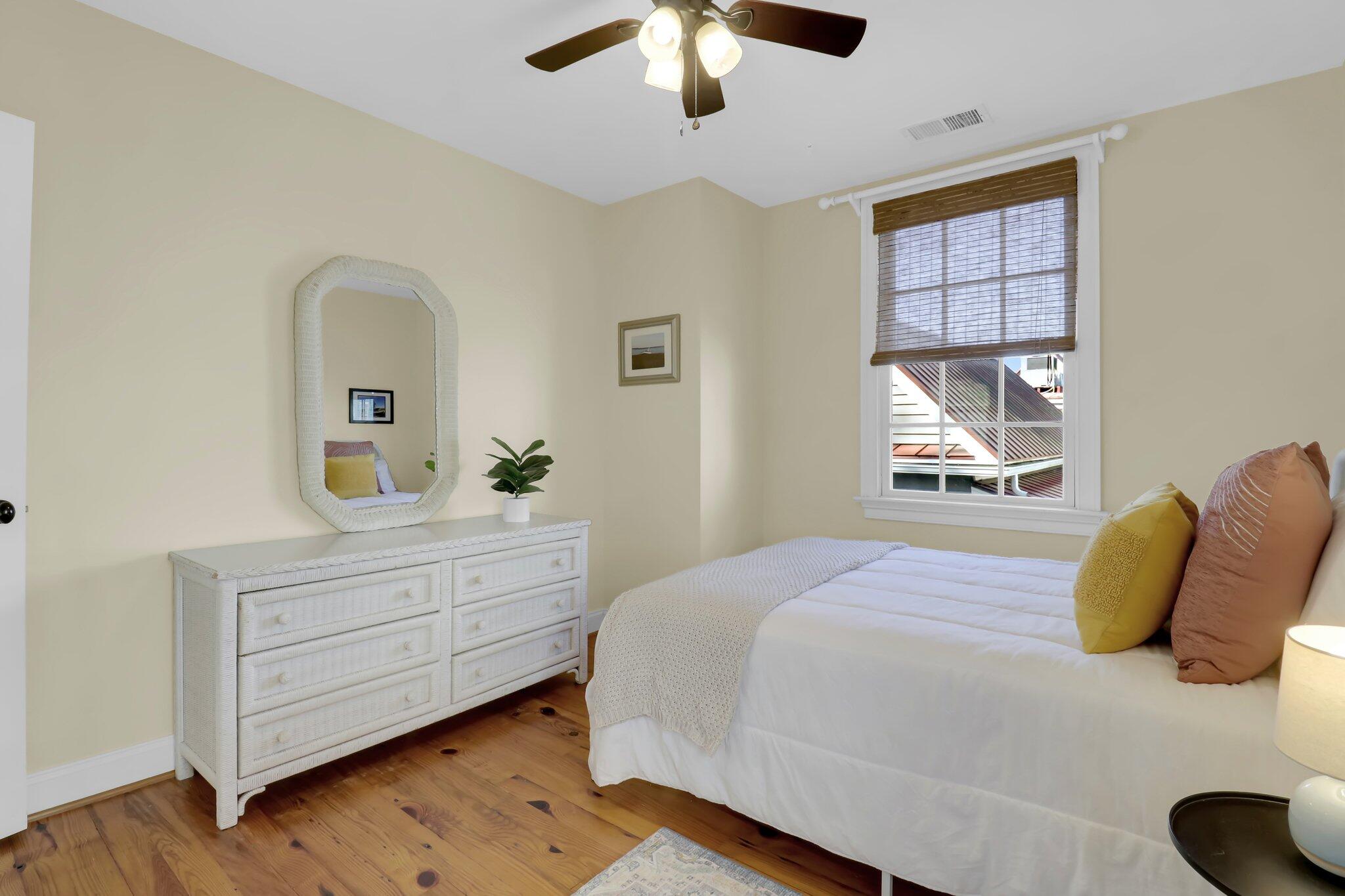 Bedroom with white bedding, colorful accent pillows, a white dresser, and warm wood floors.