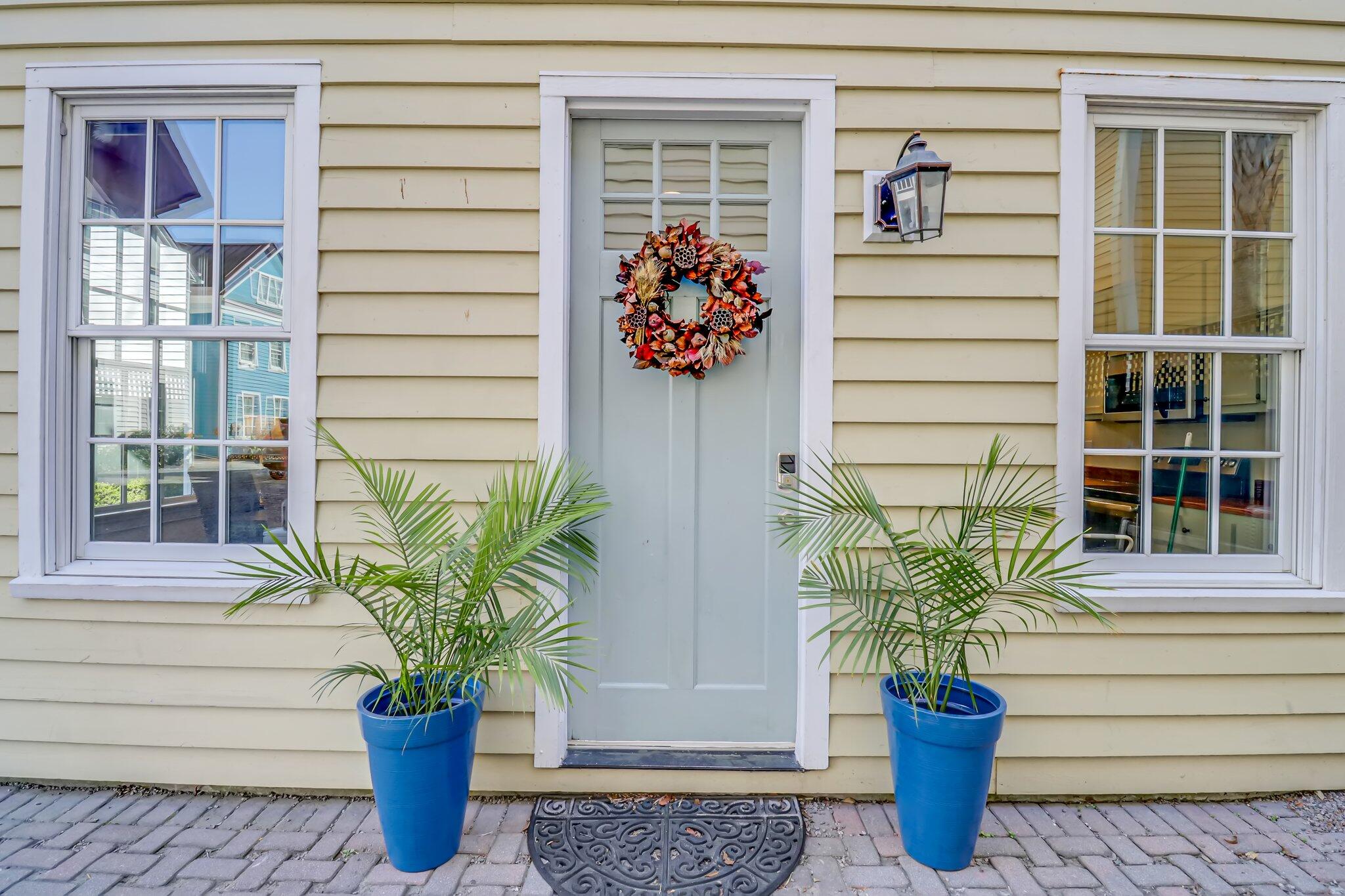 Home entrance with a blue door, autumn wreath, white-trimmed windows, and potted palms.