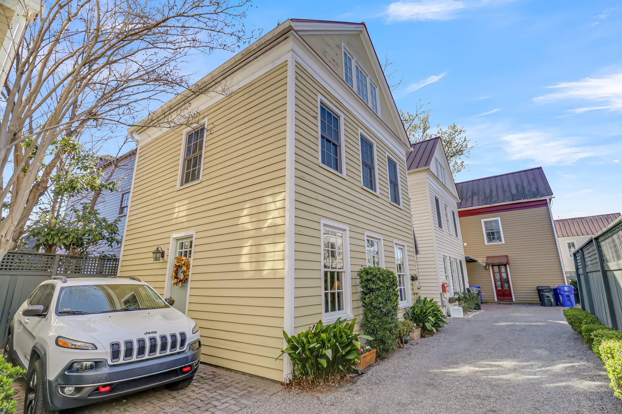Yellow clapboard house with white trim beside a gravel driveway and parked Jeep.