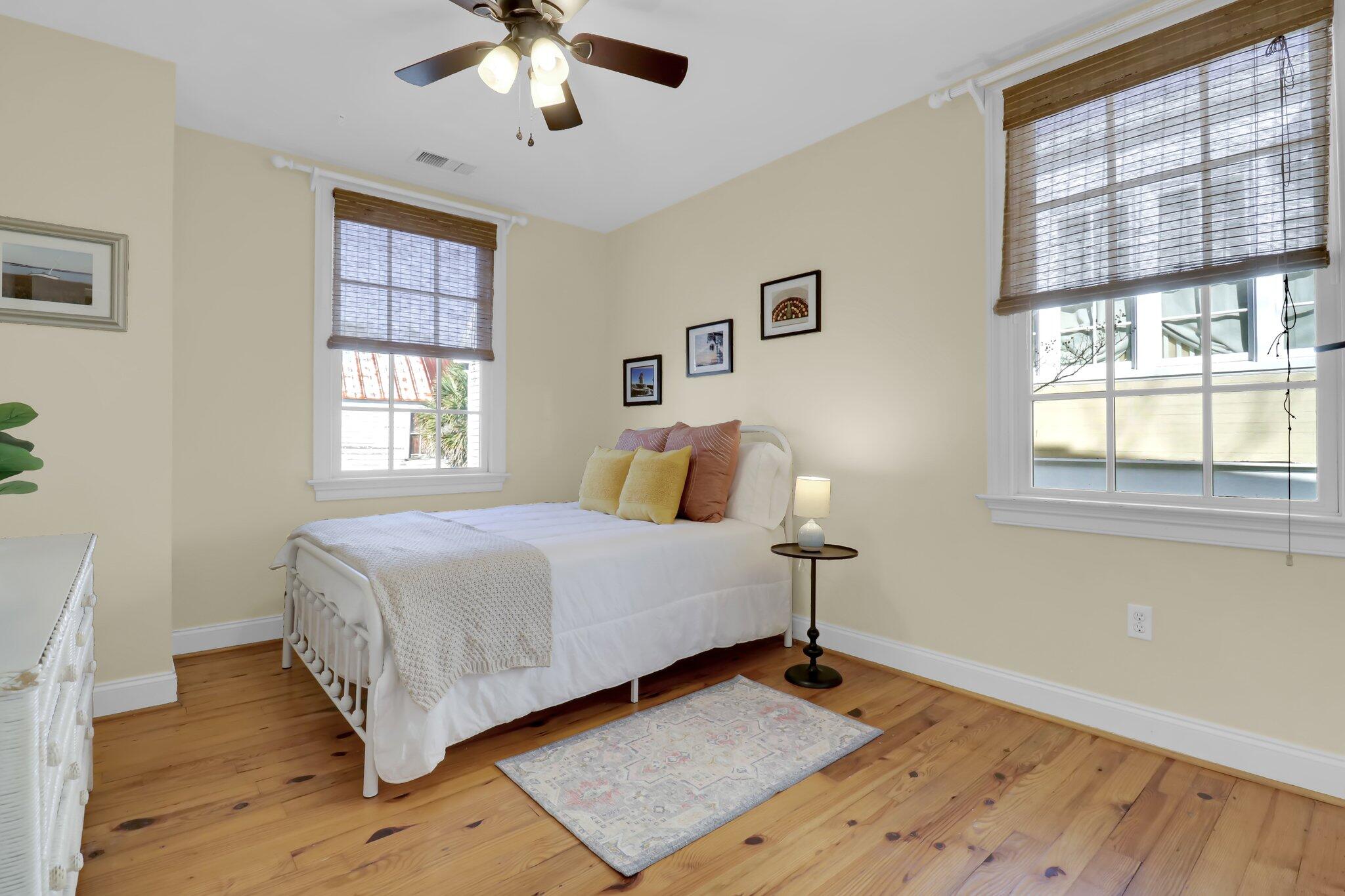 Bedroom with a white bed, colorful pillows, bamboo blinds, and warm wood floors.