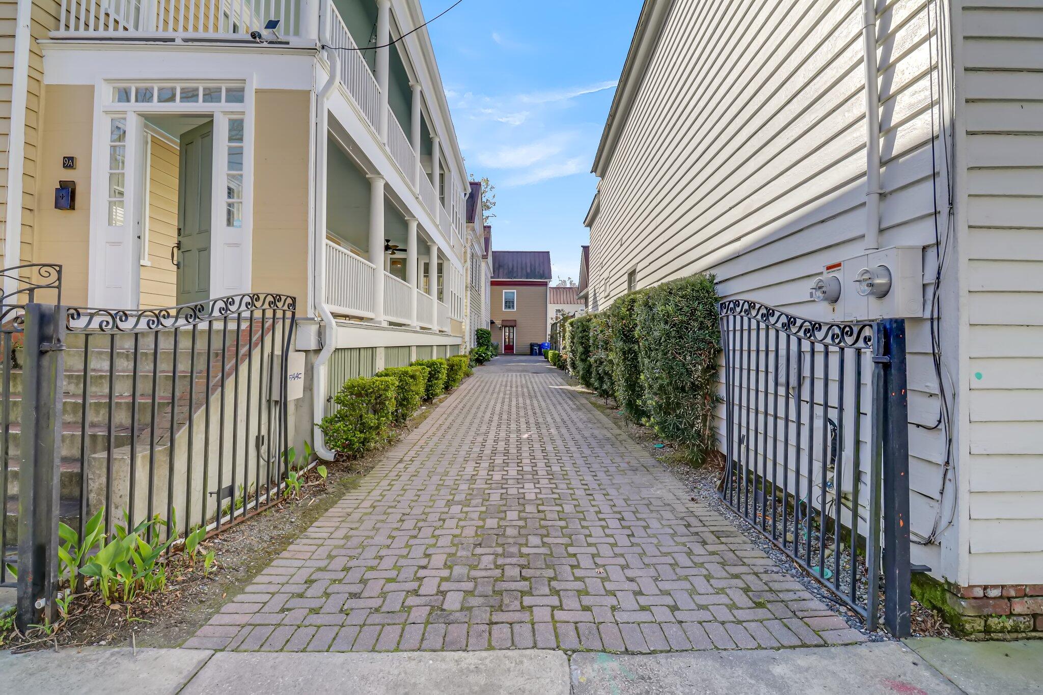 Brick-paved walkway between residences, with hedges, metal gates, and a porch entrance marked 9A.