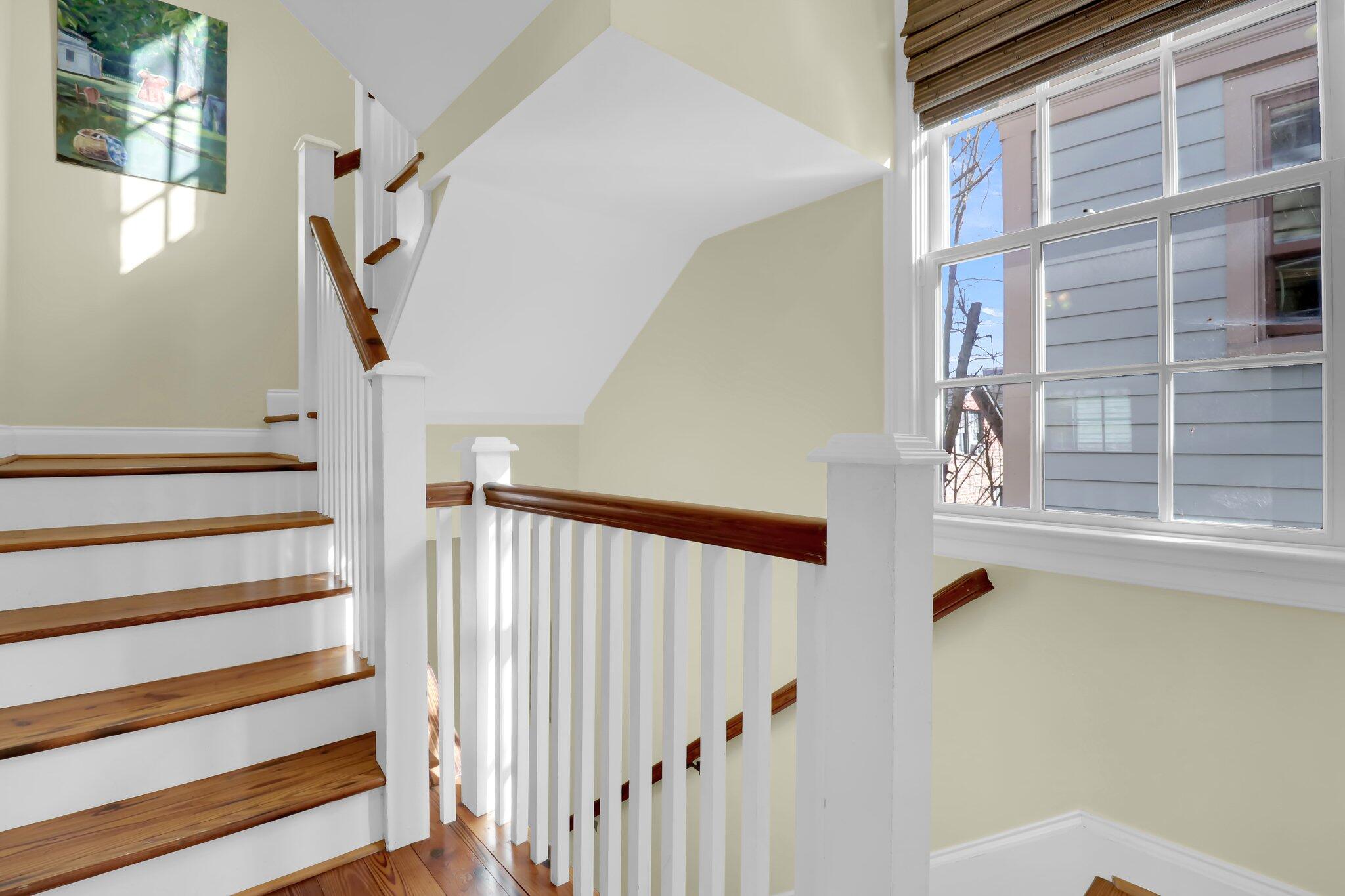 Stairwell with polished wood steps, white railings, and a large sunlit window.