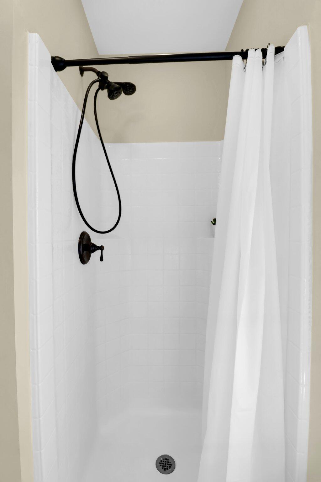 White-tiled shower with a white curtain and black handheld showerhead.