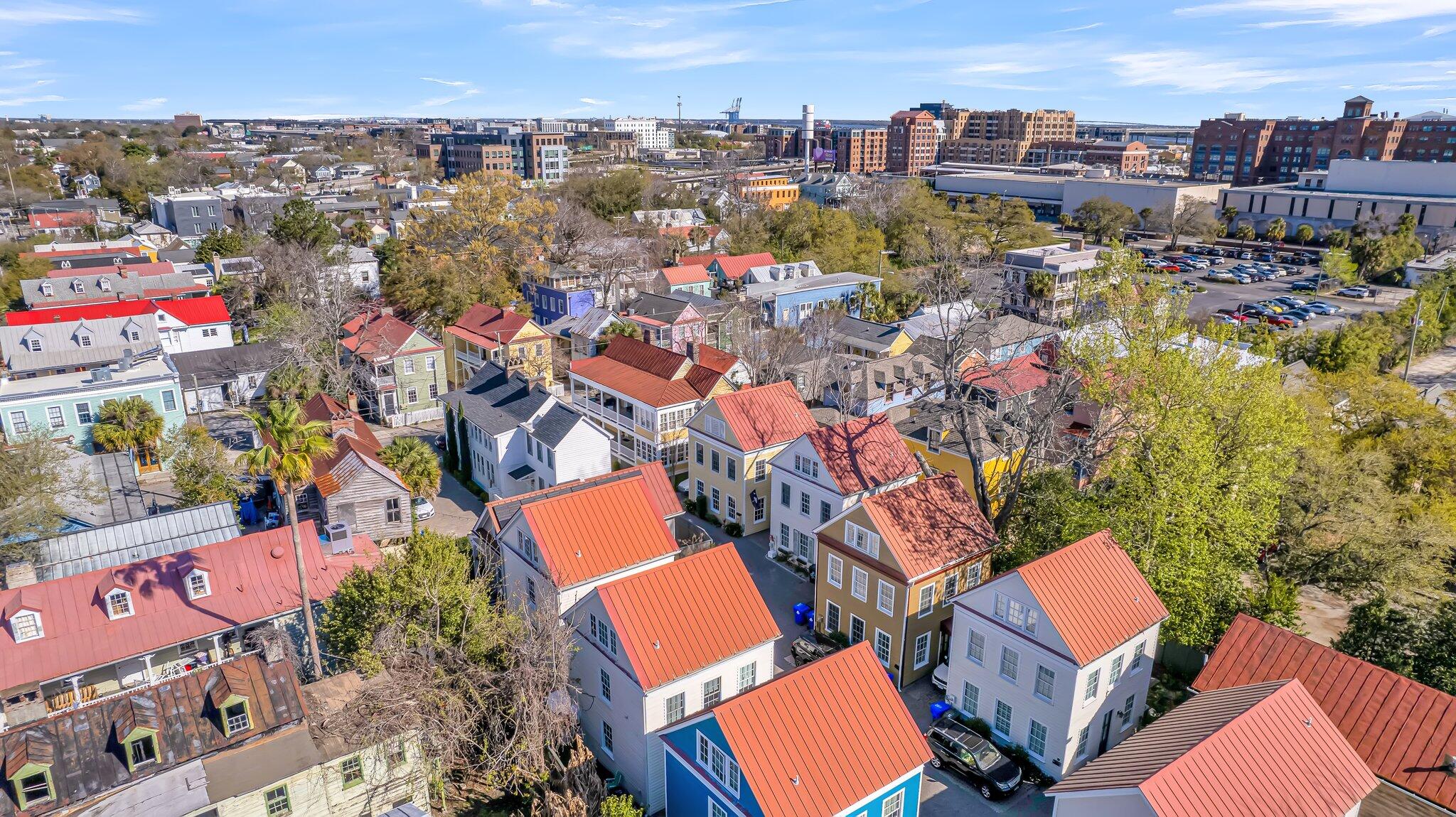 Aerial view of colorful Charleston homes with red metal roofs and downtown buildings beyond.