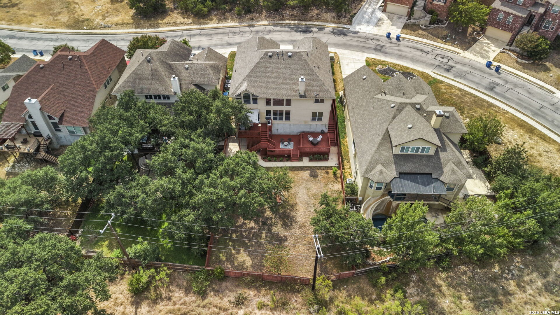 Aerial view of a two-story home with a large red deck and tree-filled backyard.