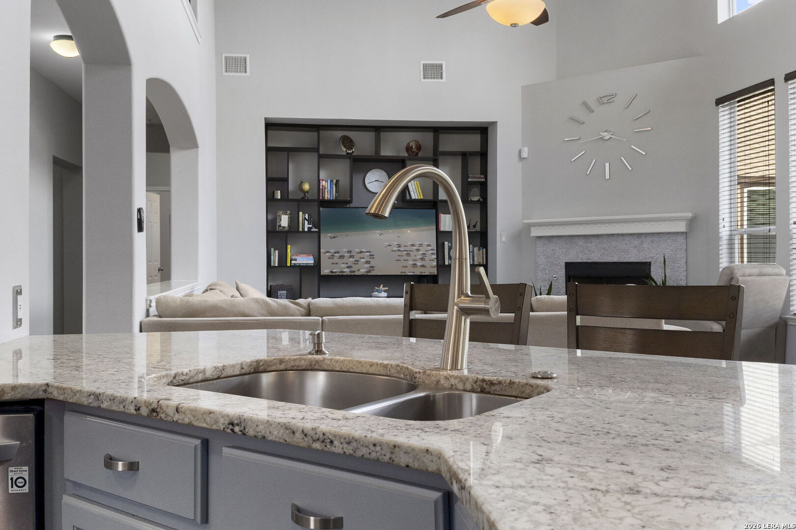 Kitchen island with granite counters and double sink overlooking a furnished living room with built-in shelving and fireplace.