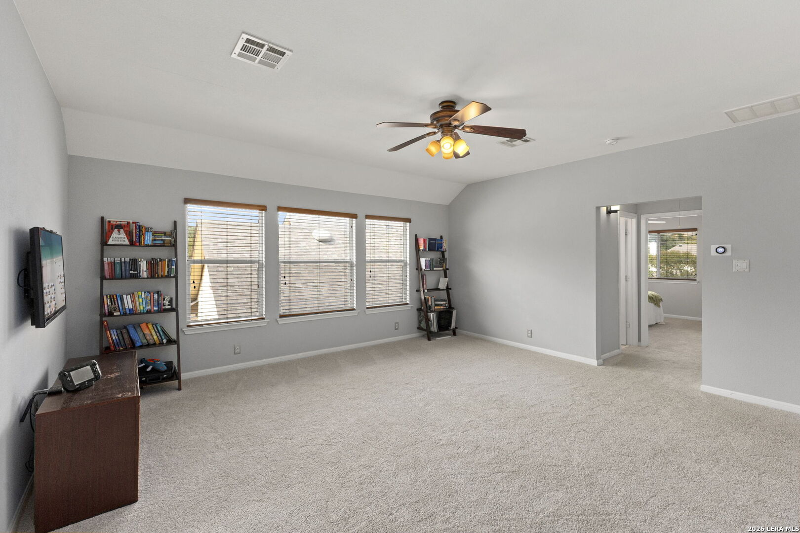 Carpeted room with three window blinds, bookshelves, a television, and a ceiling fan.