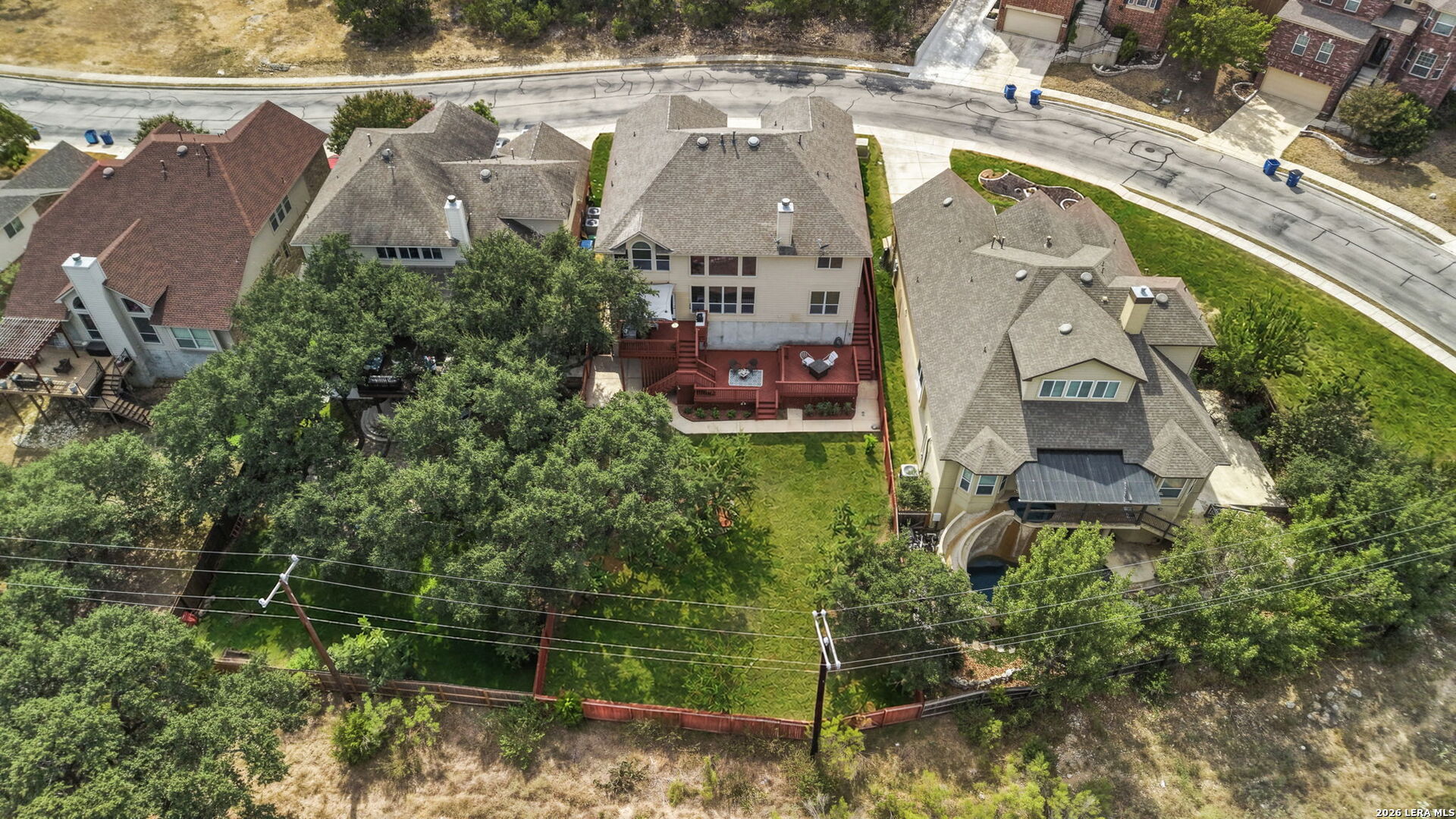 Two-story home with a large red rear deck and a fenced, tree-shaded backyard.