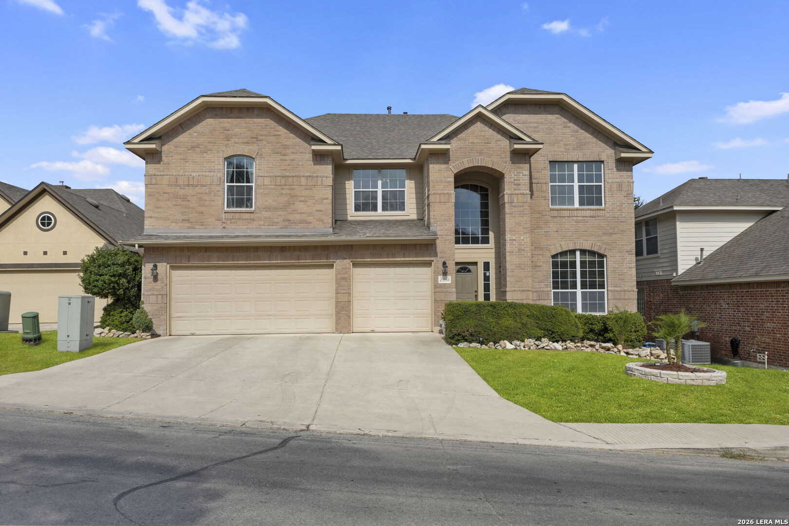 Two-story brick house with a three-car garage, arched entry, and landscaped front lawn.