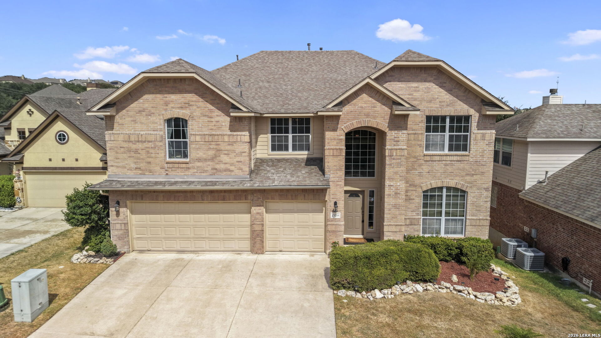 Two-story brick house with a three-car garage, arched entry, and landscaped front yard.