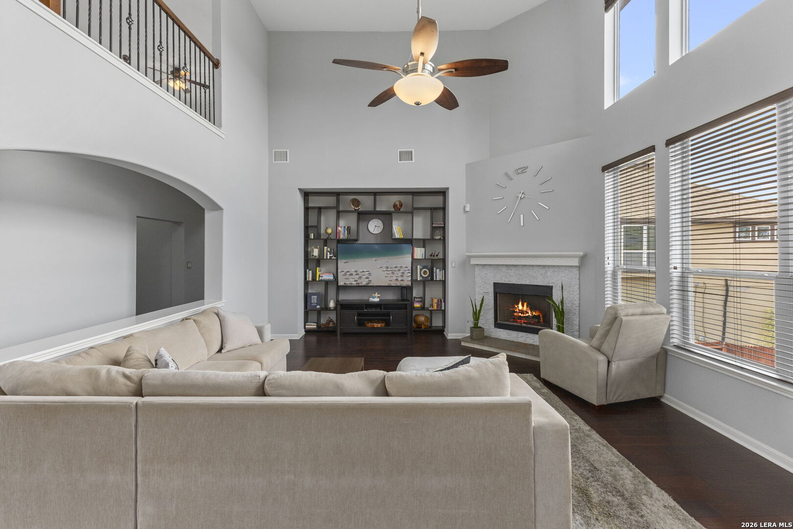 Living room with a tall ceiling, built-in shelving, and a fireplace beside large windows.