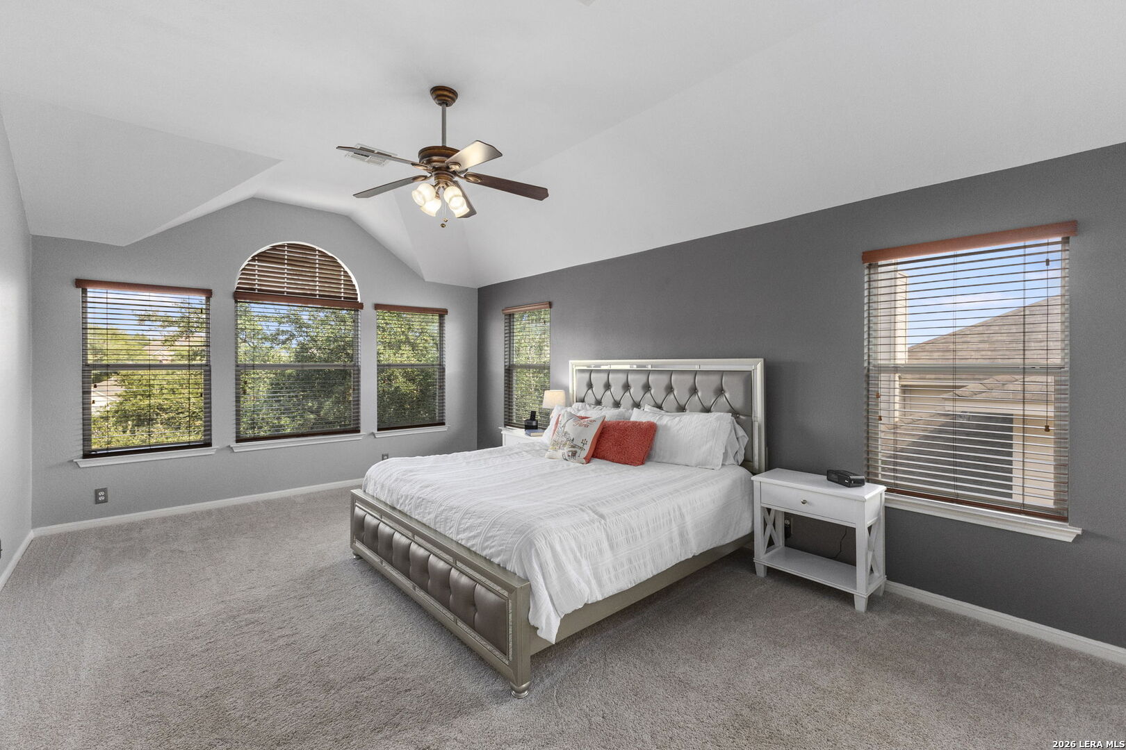 Furnished bedroom with a large bed, high angled ceiling, and windows with wooden blinds.