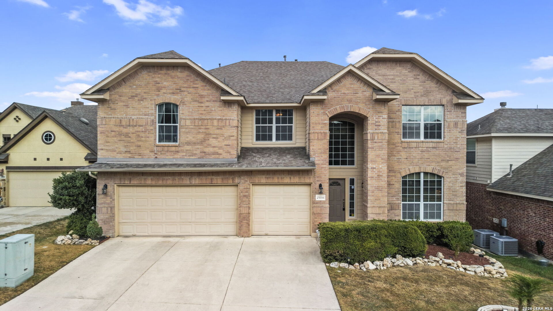 Two-story brick house with a double garage, arched entry, and trimmed front shrubs.