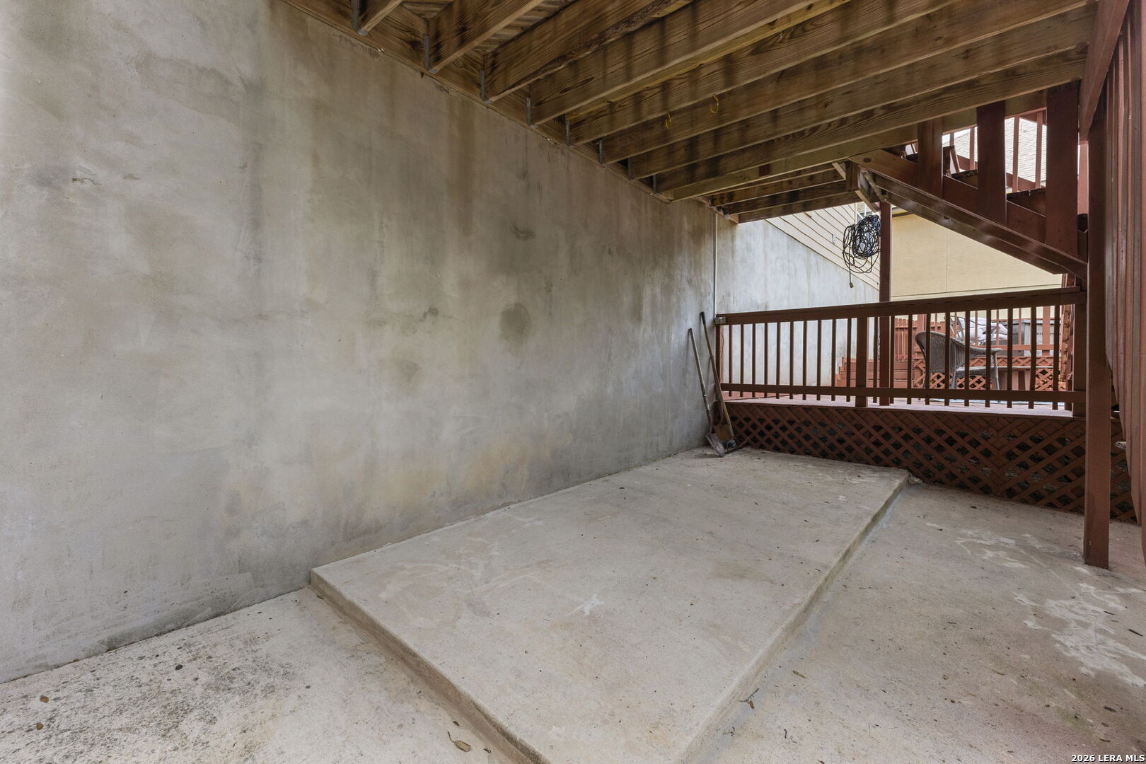 Covered concrete patio beneath a raised wooden deck with exposed joists and wood lattice railing.