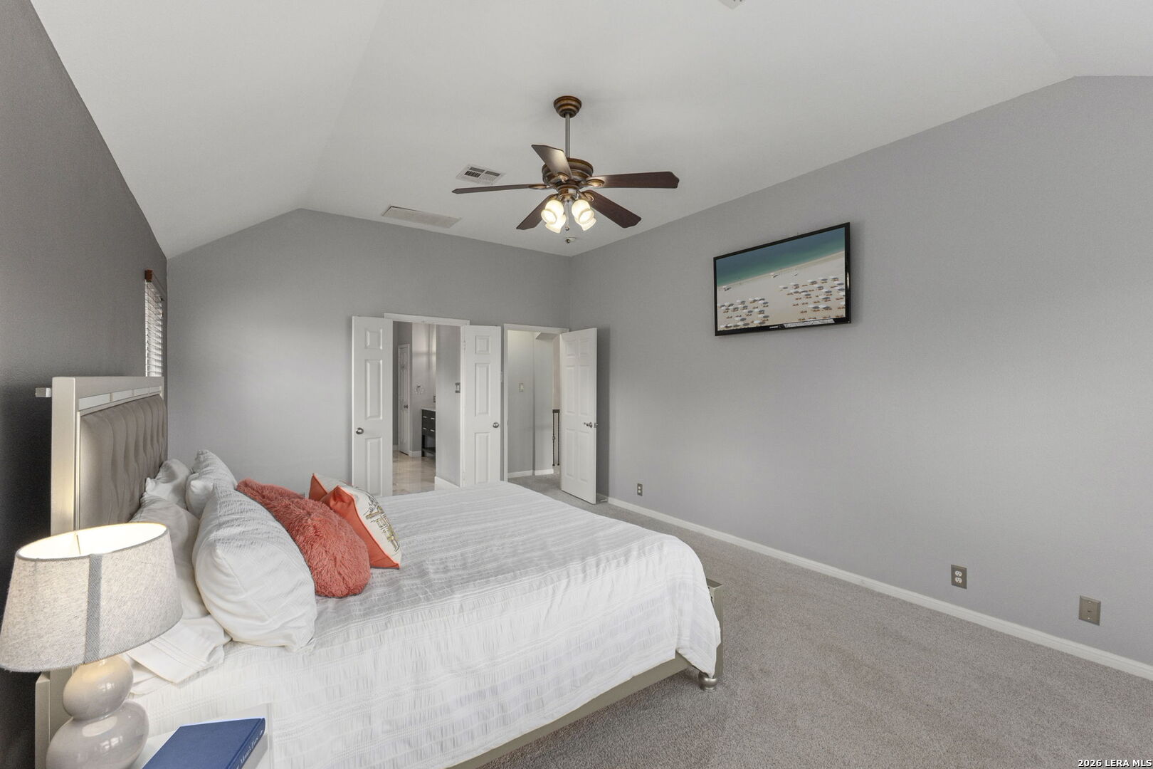 Furnished bedroom with a white bed, coral accent pillows, and a vaulted ceiling with a ceiling fan.