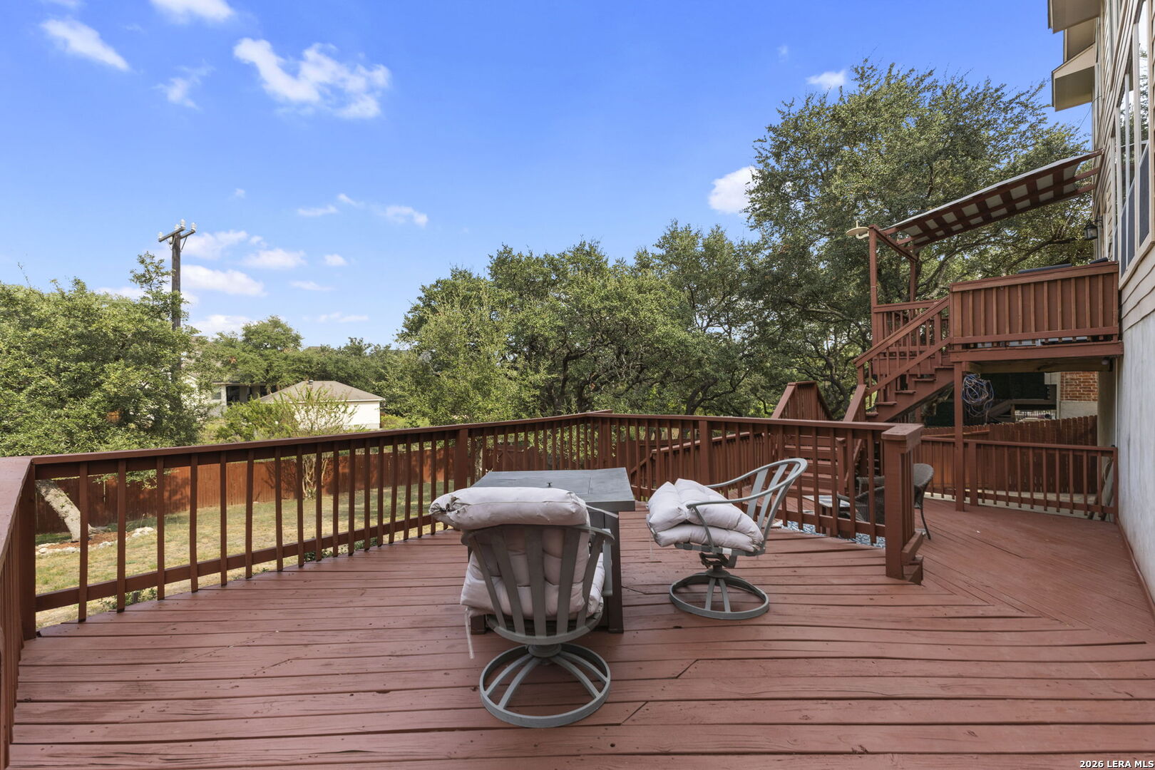 Wooden deck with cushioned seating and a table, surrounded by mature trees.