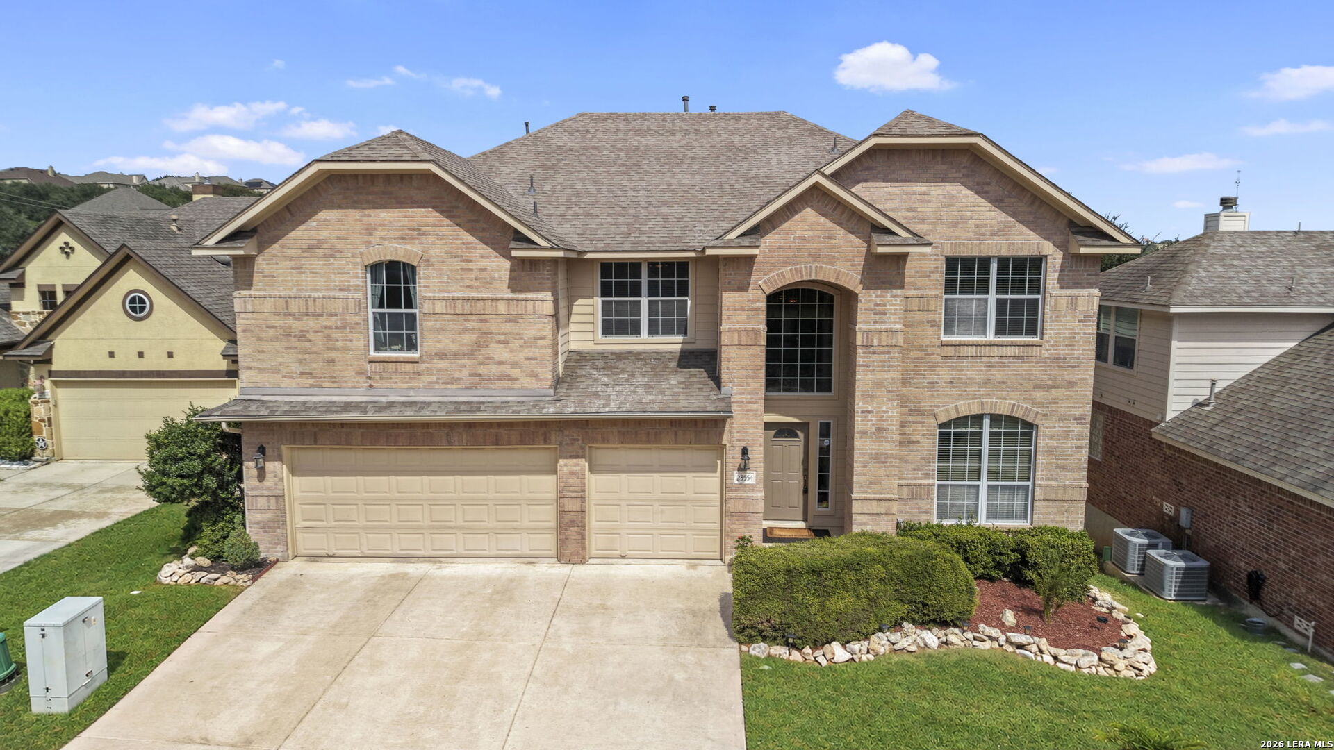 Two-story brick home with an arched entry, three-car garage, and landscaped front yard.