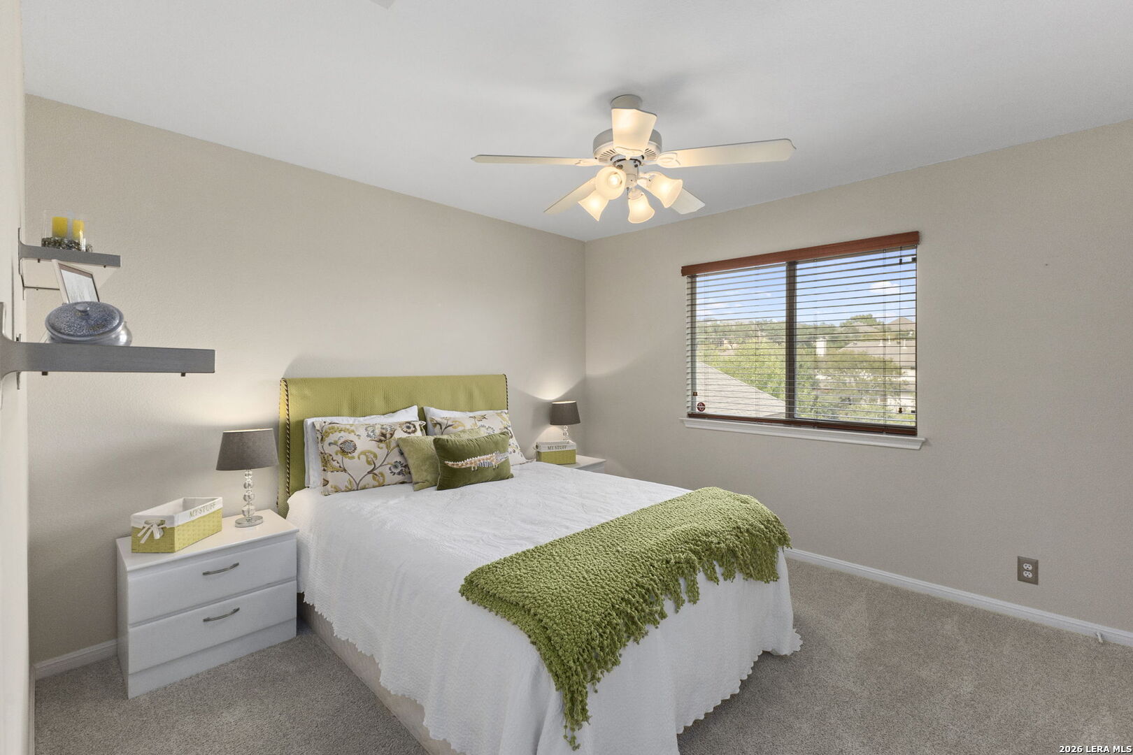 Furnished bedroom with a green headboard and throw, white bedding, and a window with wooden blinds.