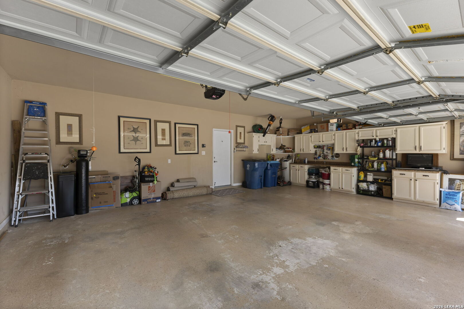 Garage with open overhead door, concrete floor, and extensive storage cabinets along the back wall.