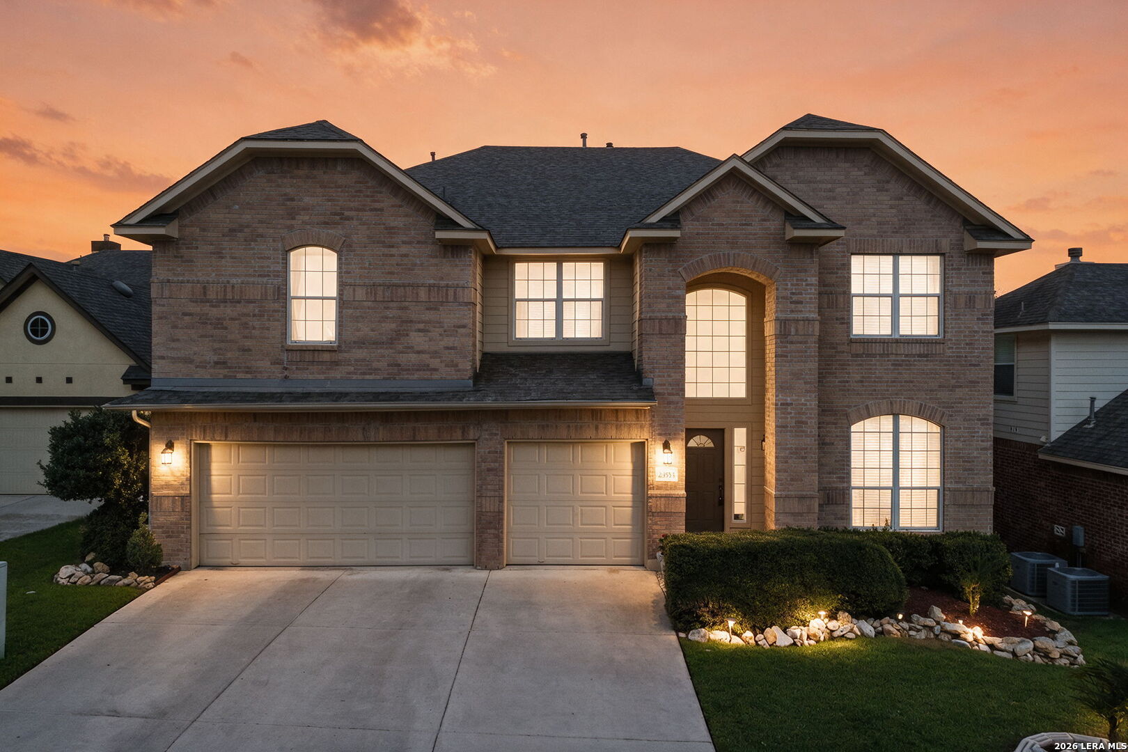 Two-story brick house with a three-car garage and arched entry, photographed at dusk.
