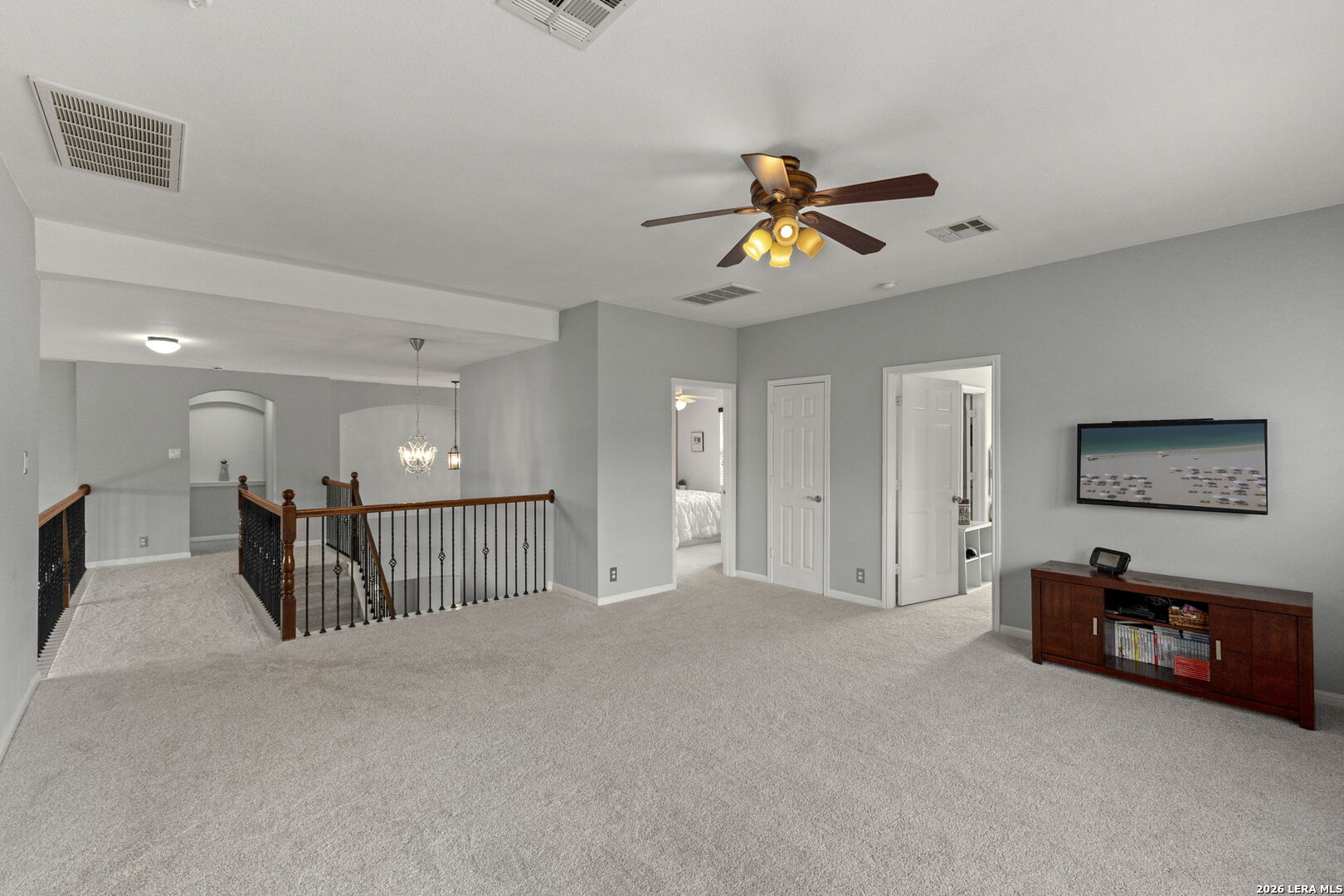 Carpeted upstairs loft with a wrought-iron railing, ceiling fan, and television console.