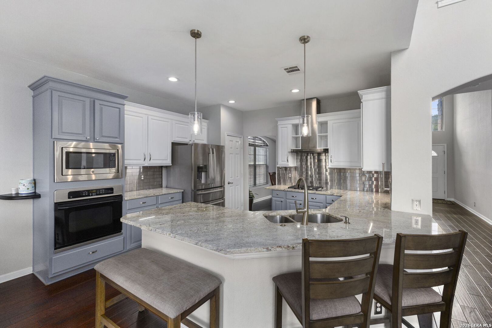 Kitchen with blue-gray cabinetry, stainless steel appliances, and a large granite island with a double sink.