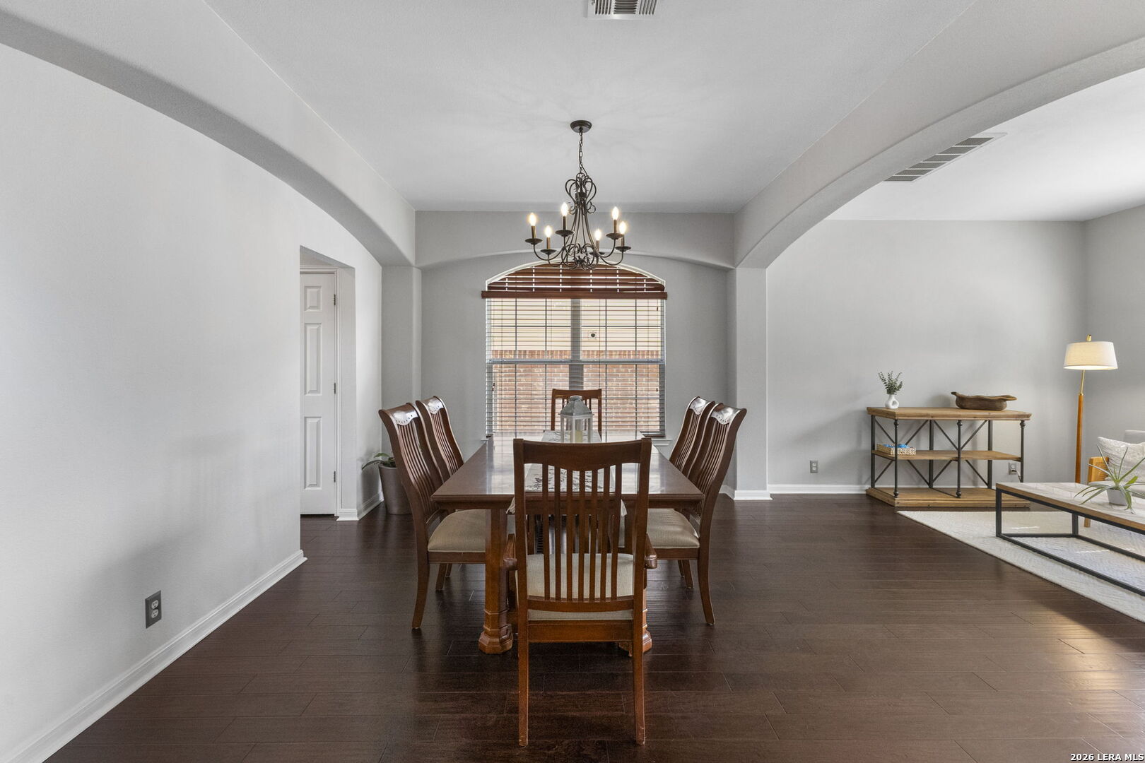 Dining room with a dark wood table, chandelier, and arched window with blinds.