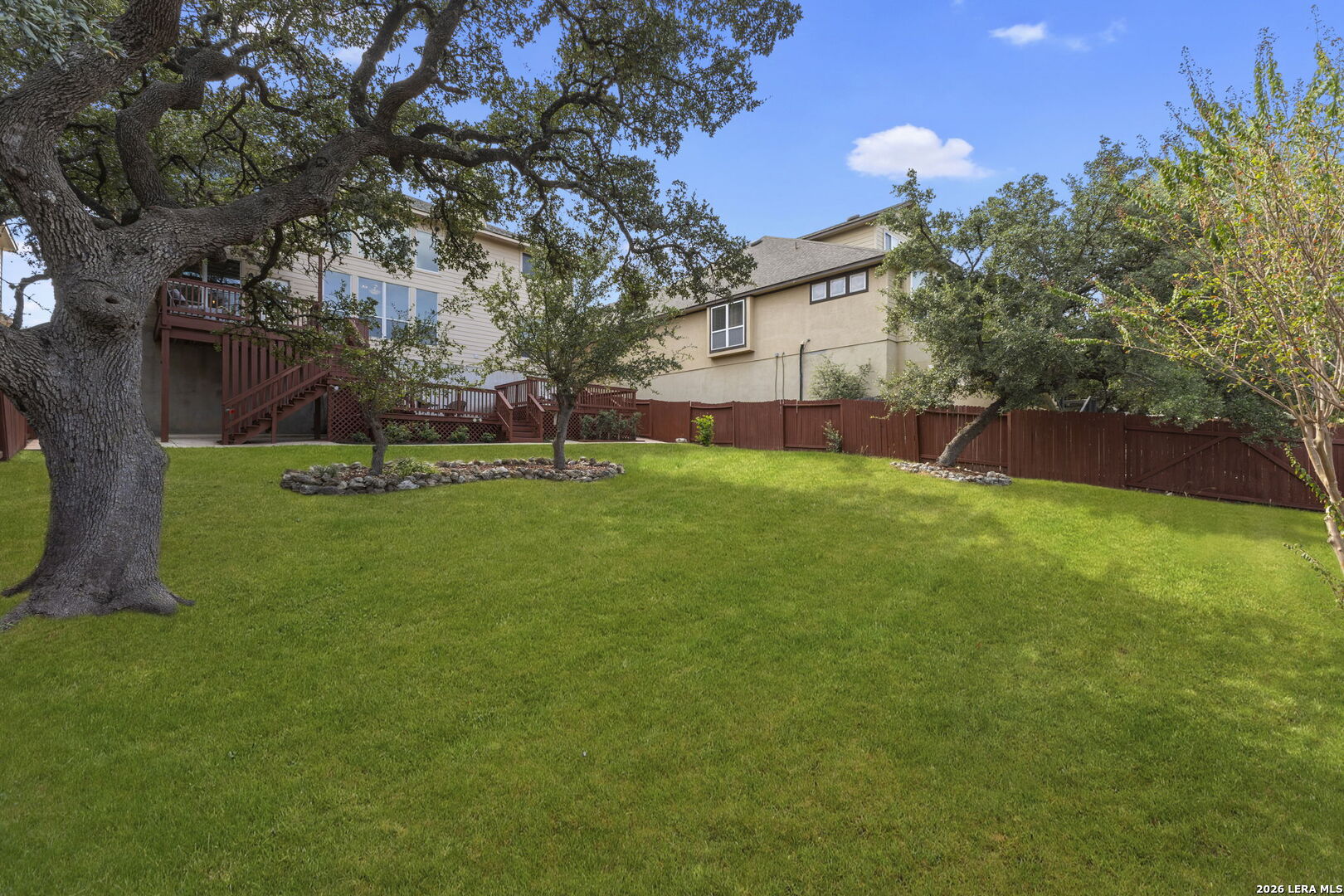 Backyard with a broad green lawn, mature shade trees, privacy fencing, and a raised wooden deck.