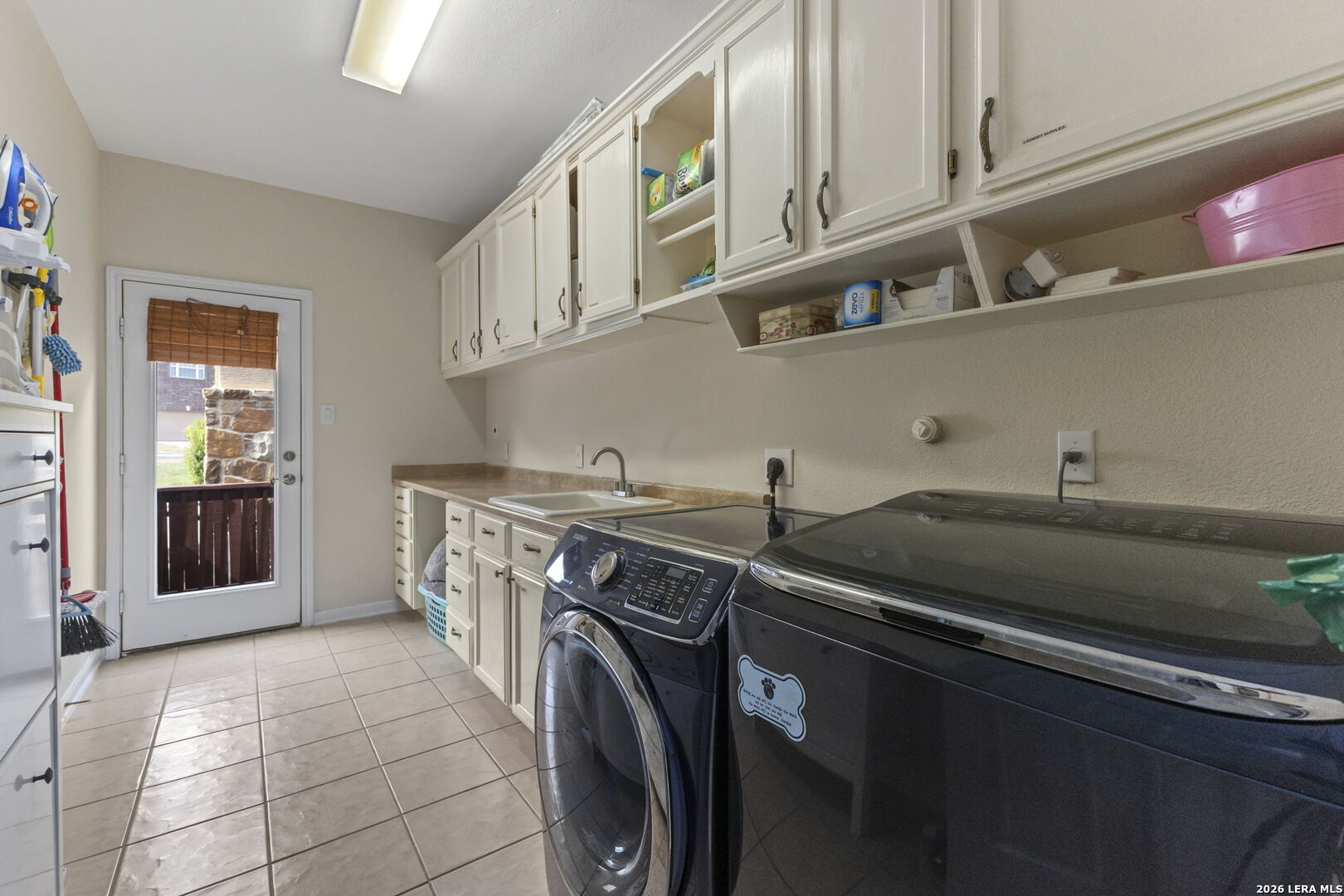 Laundry room with front-loading washer and dryer, white cabinets, utility sink, and exterior door.