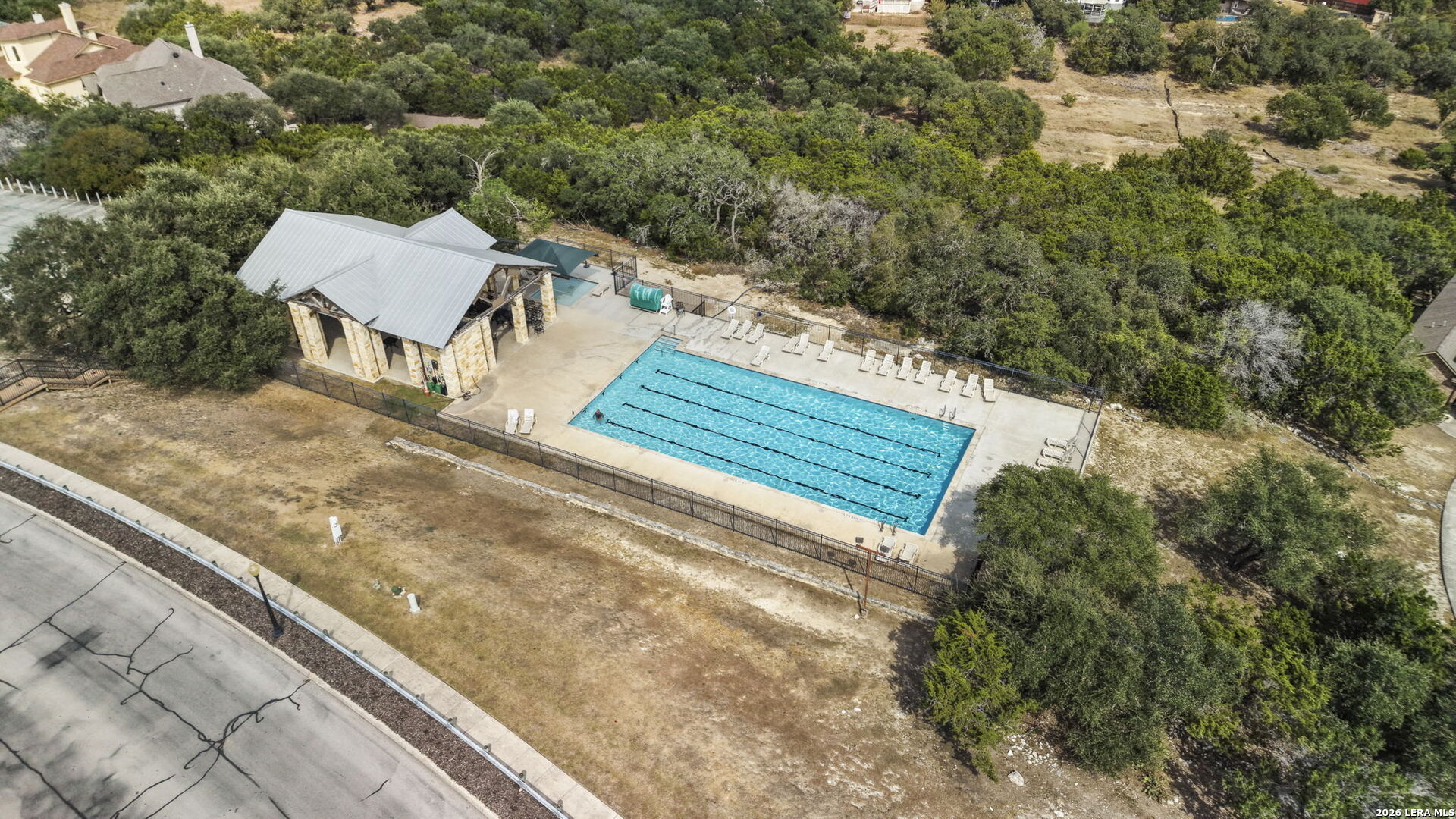 Community pool with lane markings, a stone pavilion, and loungers surrounded by trees.