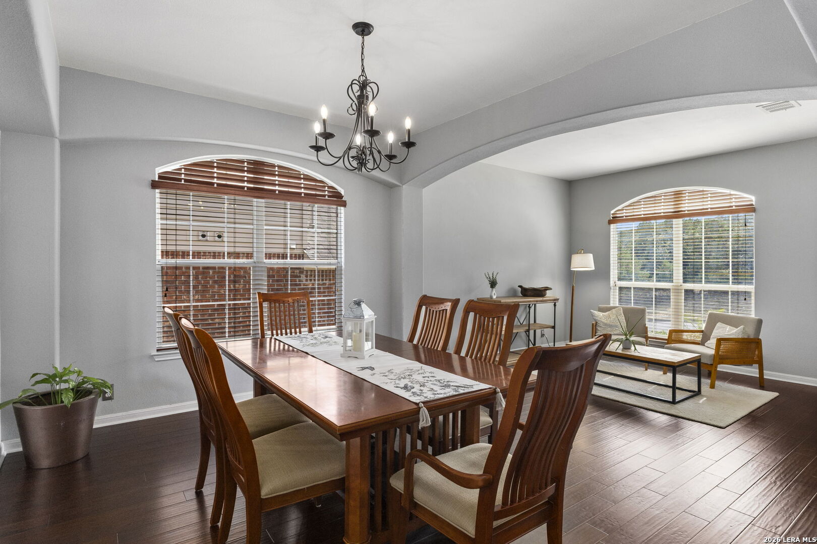 Dining room with a long wooden table beneath a chandelier, adjoining a bright sitting area.