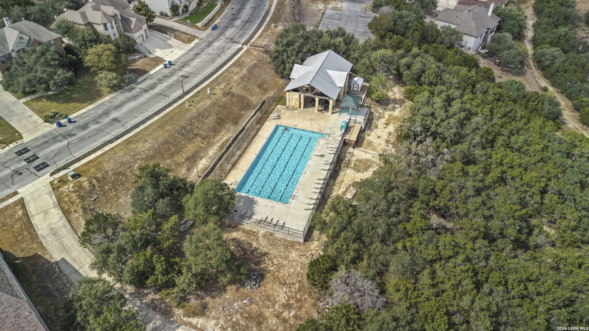 Aerial view of a neighborhood pool, with a covered pavilion and wooded surroundings.