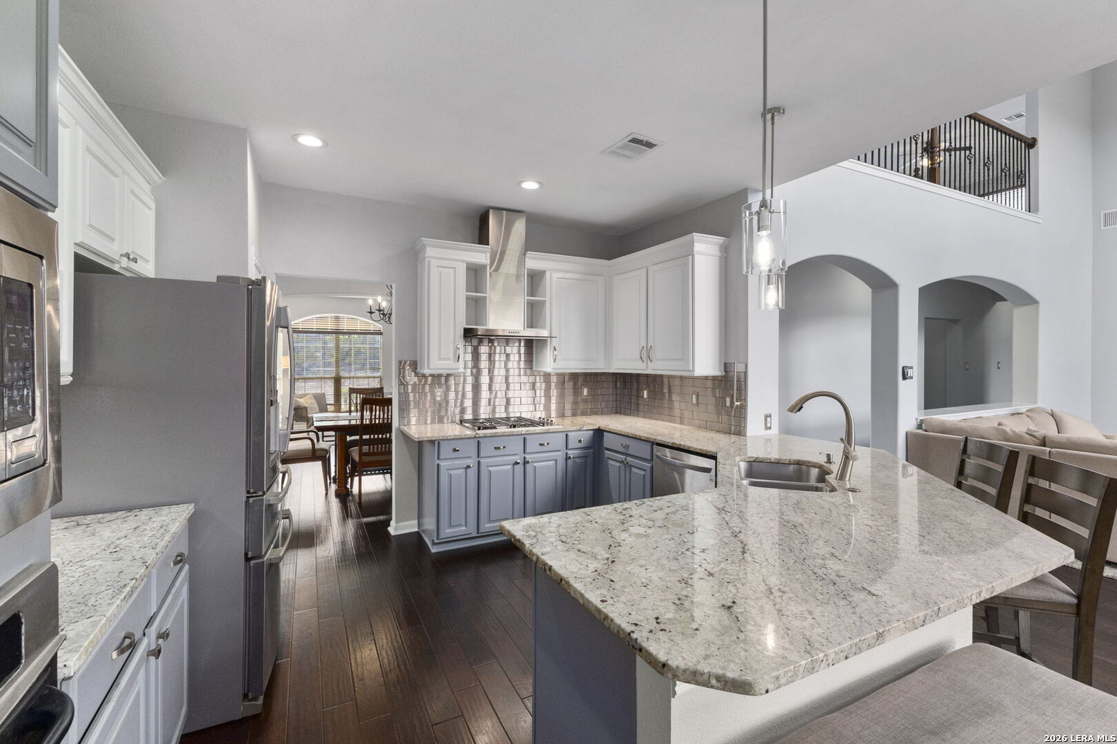 Open kitchen with blue lower cabinets, stainless steel appliances, and a large granite island.
