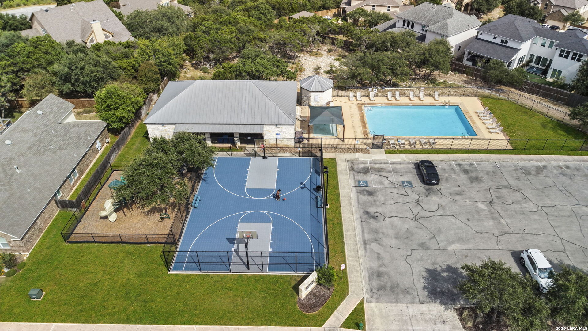 Aerial view of a neighborhood pool, basketball court, clubhouse, and parking lot.