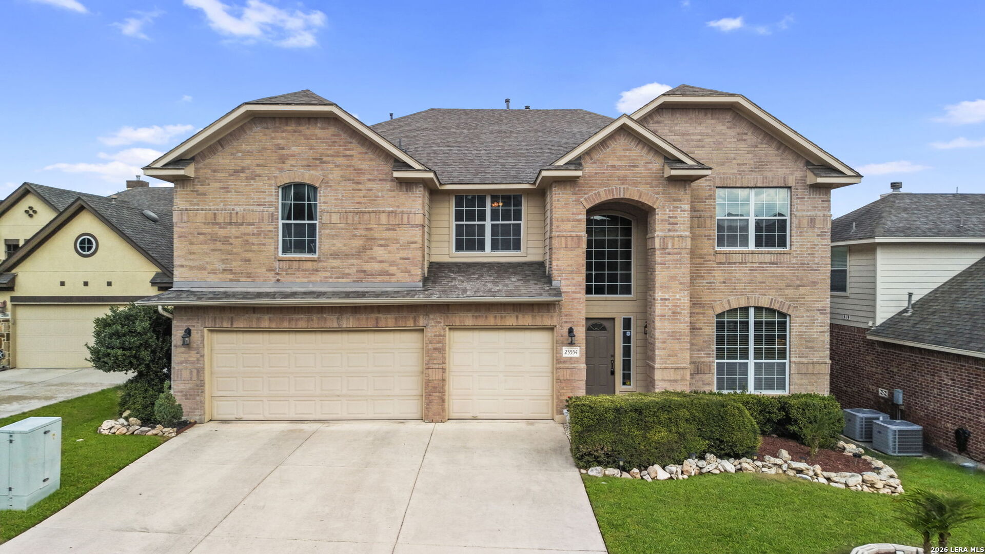 Two-story brick home with a three-car garage, arched entry, and trimmed front shrubs.