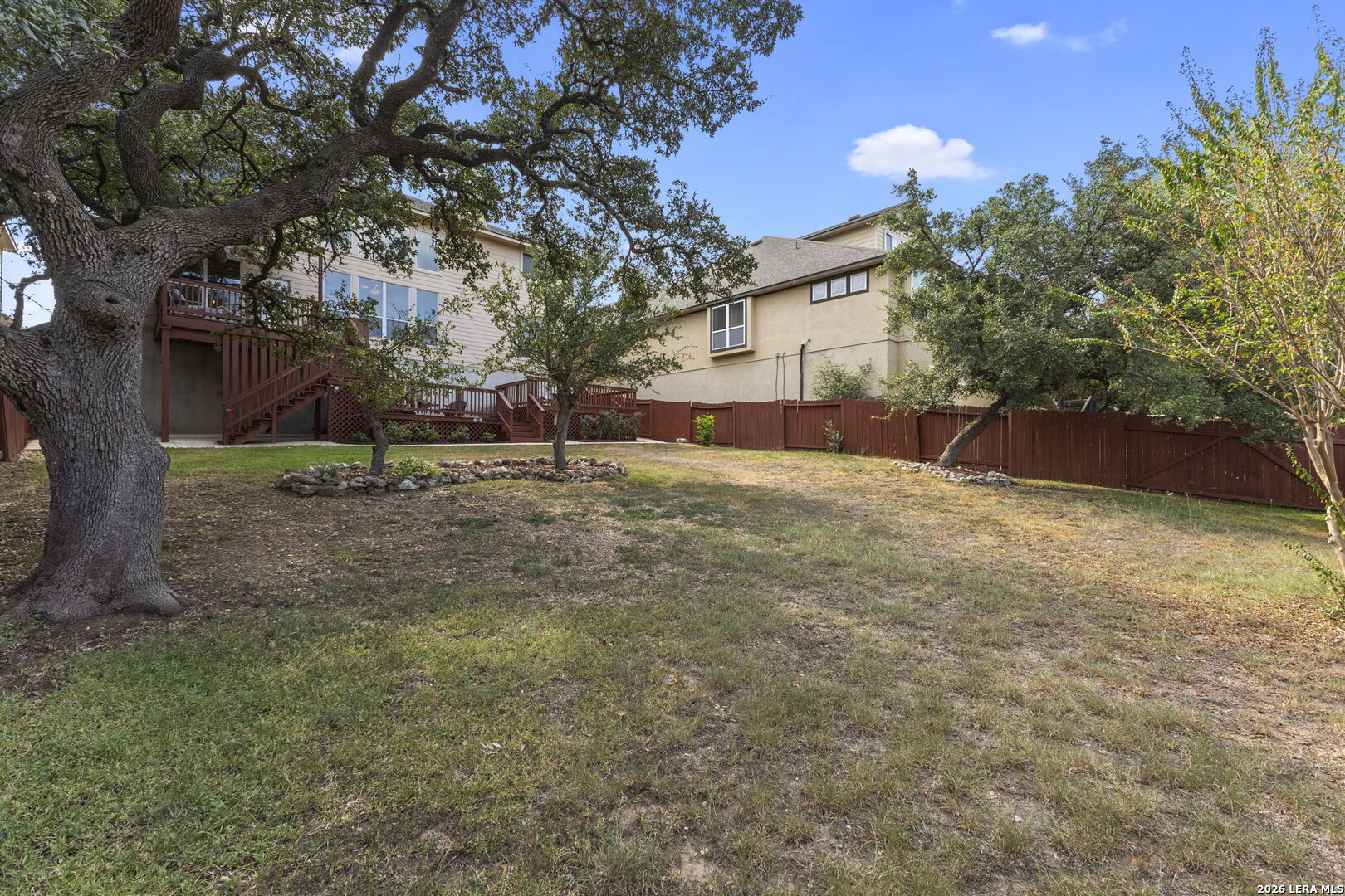 Fenced backyard with mature trees, a raised deck, and stairs behind a two-story home.
