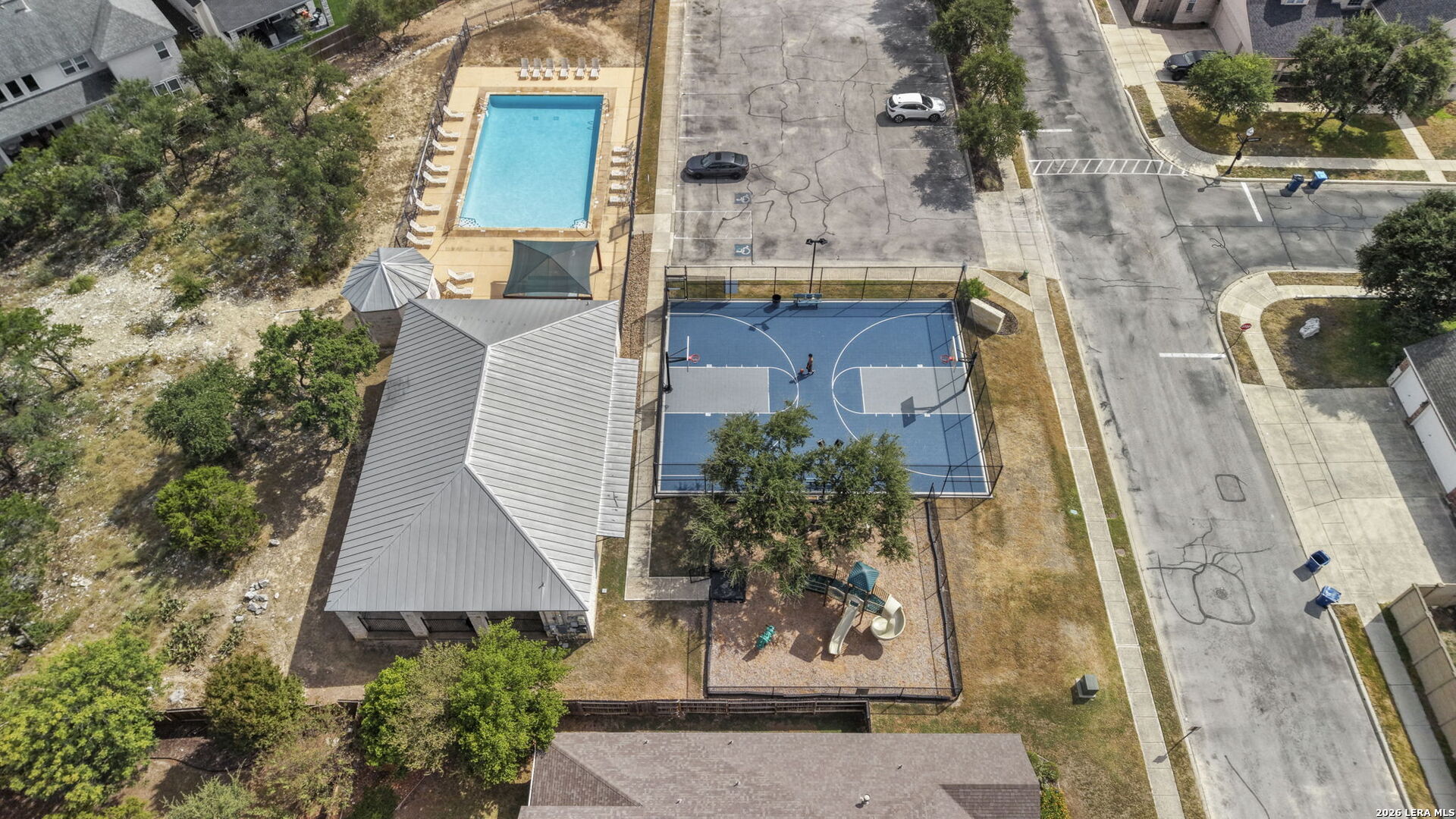 Aerial view of community amenities with a swimming pool, basketball court, playground, and clubhouse.