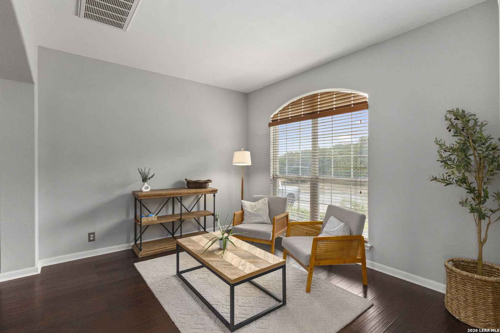 Sitting area with two gray armchairs, a wood coffee table, dark floors, and an arched window.