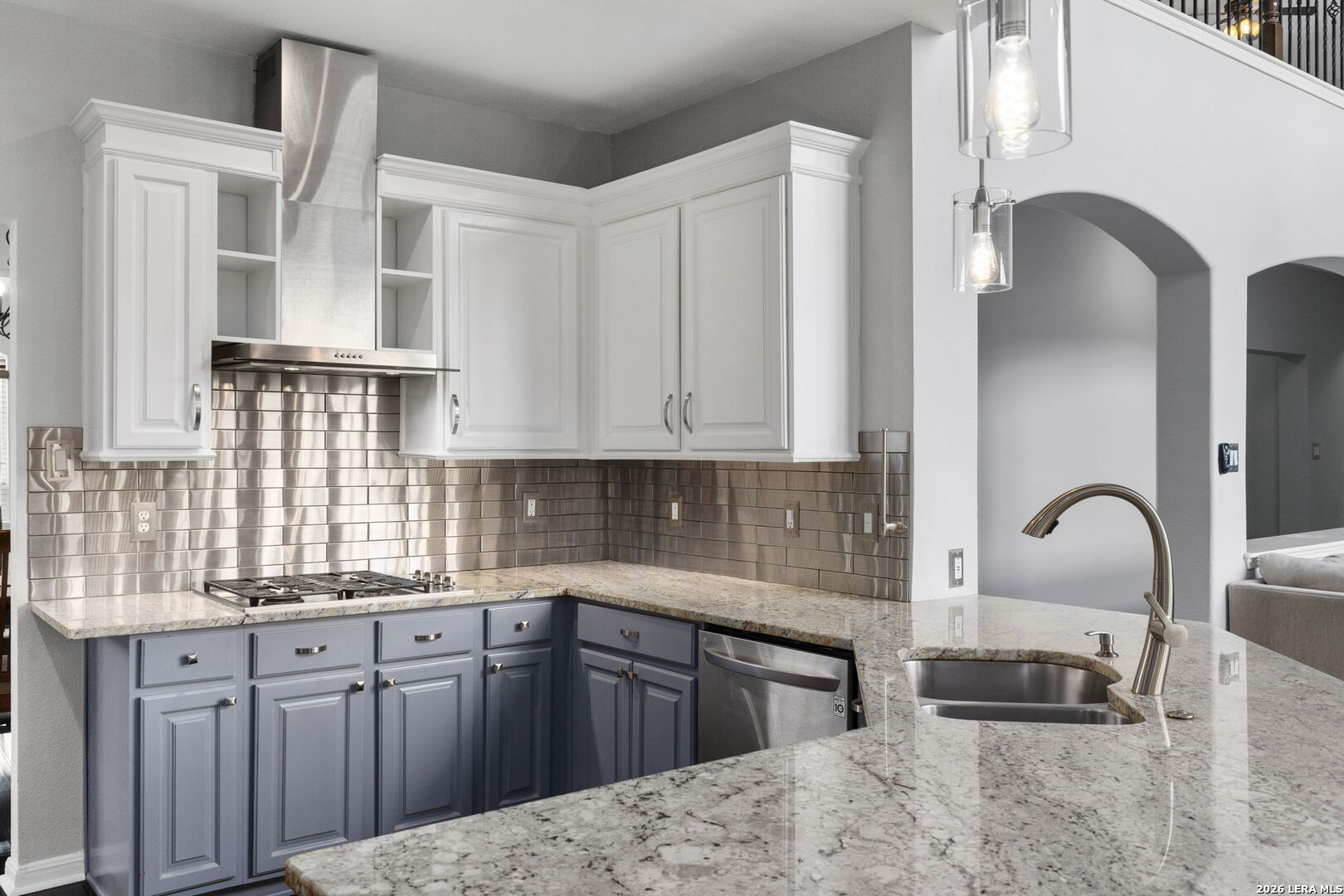 Kitchen with blue lower cabinets, granite counters, stainless steel backsplash, and a large island sink.
