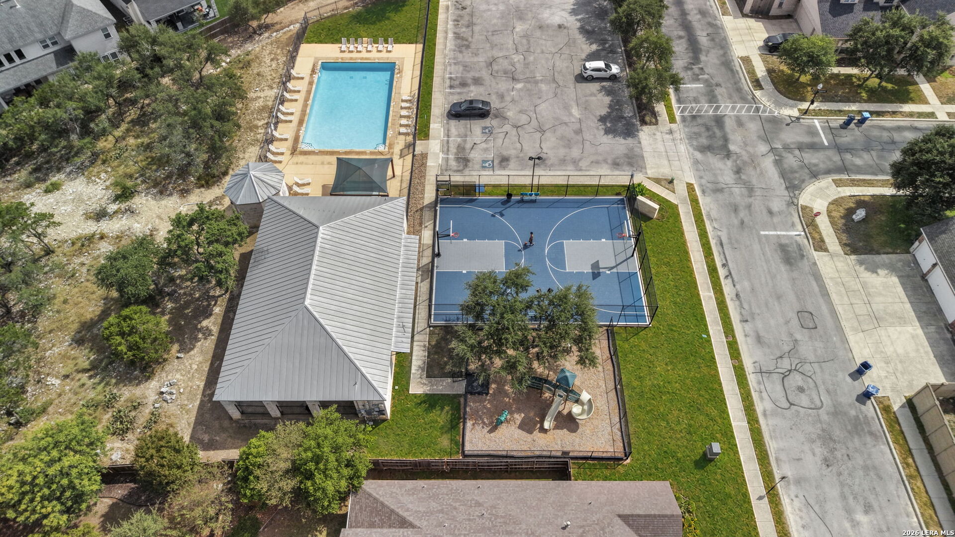 Aerial view of a community pool, basketball court, playground, and pavilion.