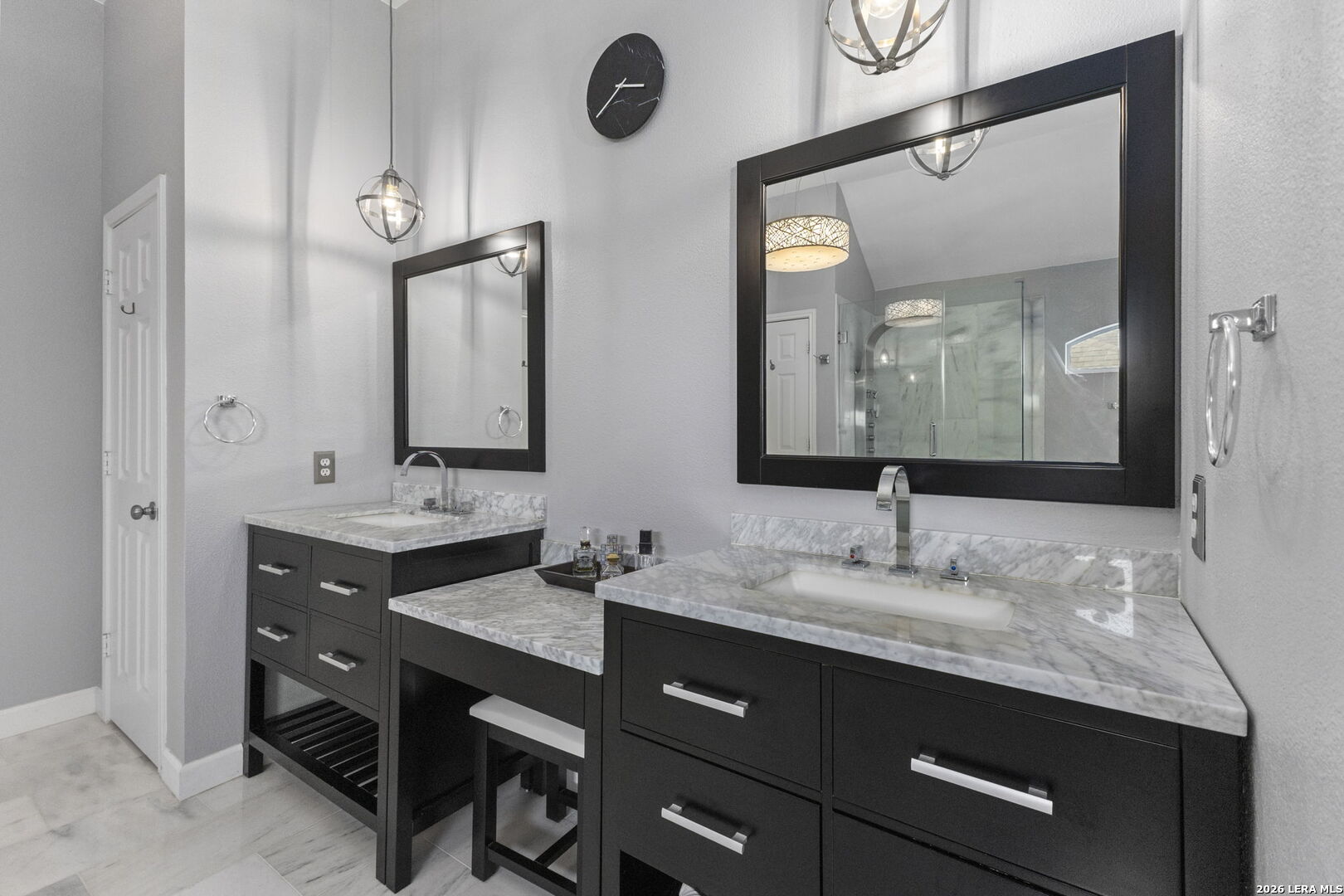 Bathroom with two dark vanities, marble countertops, and a glass-enclosed shower.