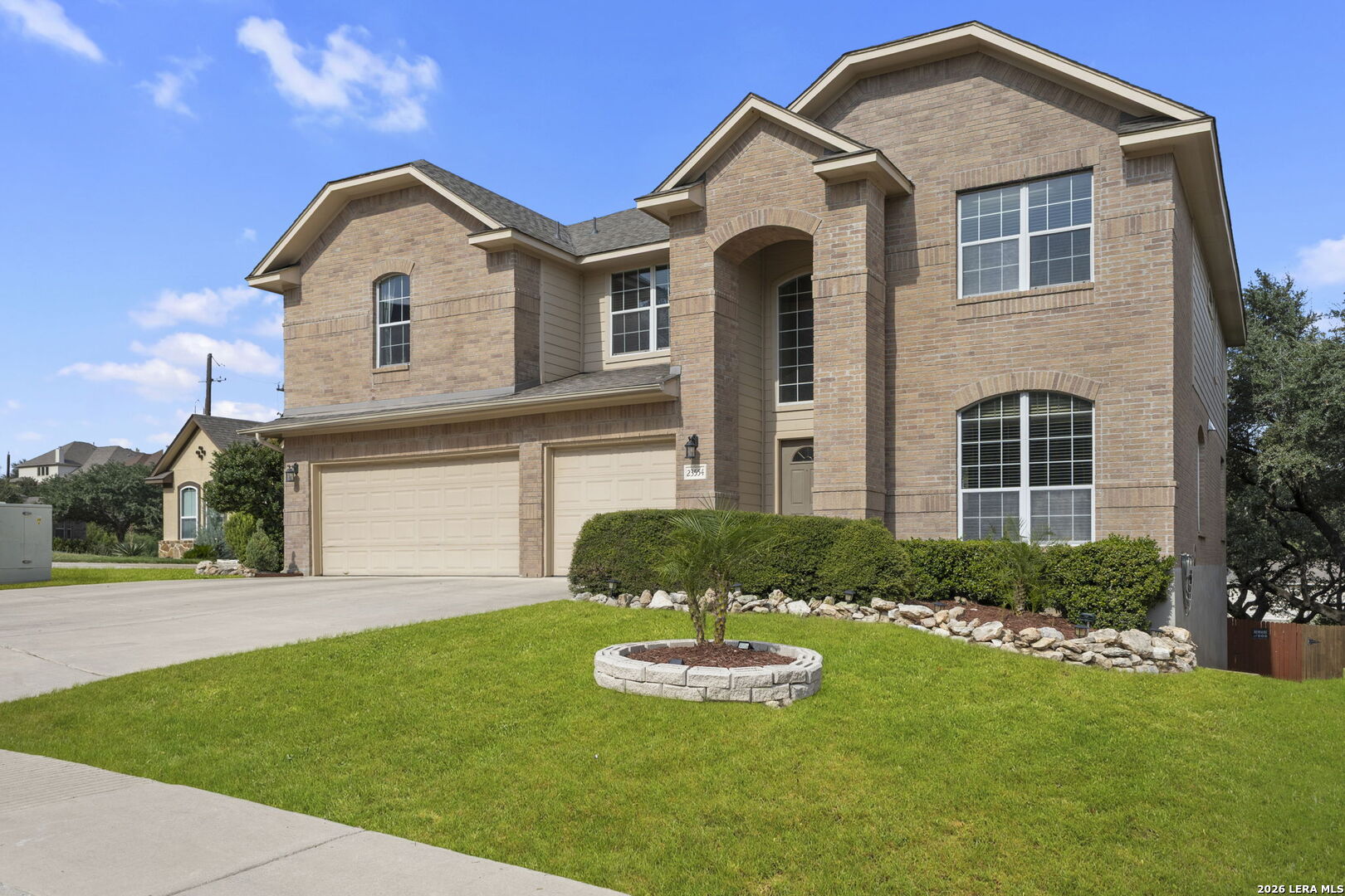Two-story brick house with an arched entry, two garage doors, and a landscaped front lawn.