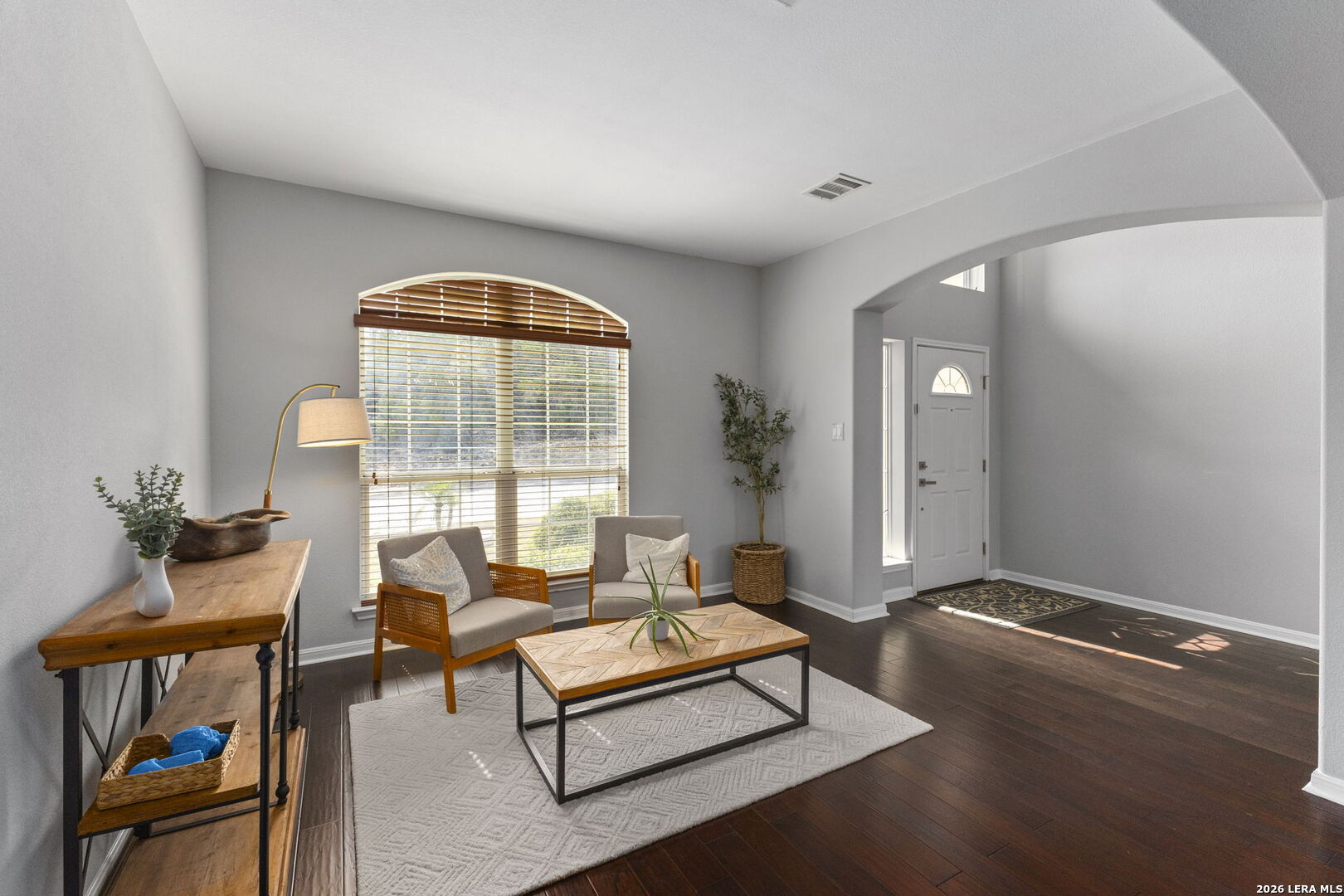 Furnished living room with an arched window, two chairs, and dark hardwood floors.