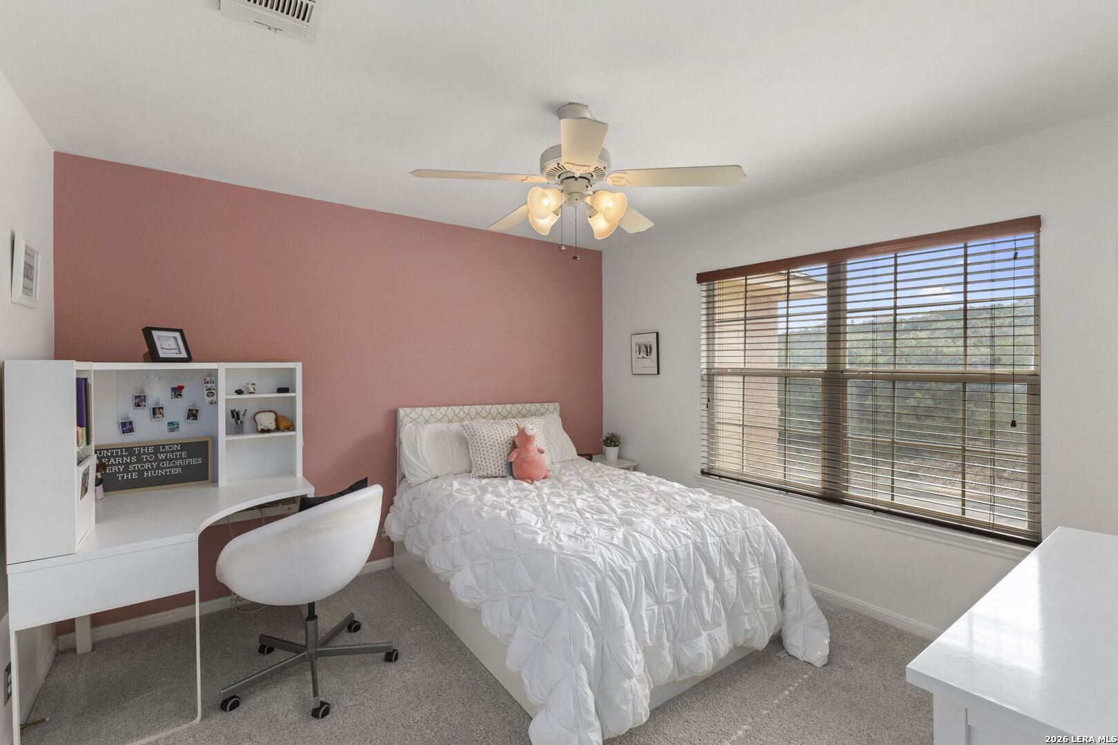 Bedroom with a white bed, pink accent wall, desk, and large window with wood blinds.